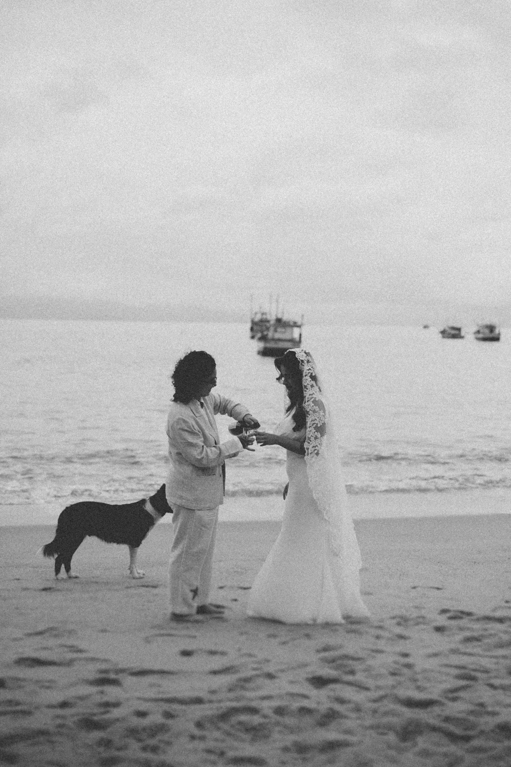 Rafaela and Nathalia share a moment on the beach at Pouso das Flores in Paraty, Brazil, as a dog watches nearby.