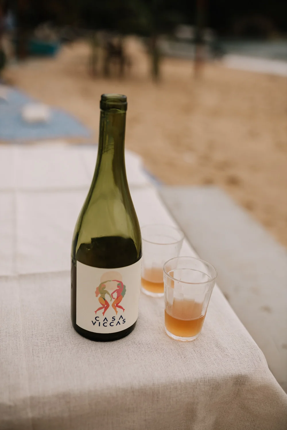 Casa Viccas wine bottle with two amber-filled glasses on a linen-draped table at Pouso das Flores in Paraty, Brazil.