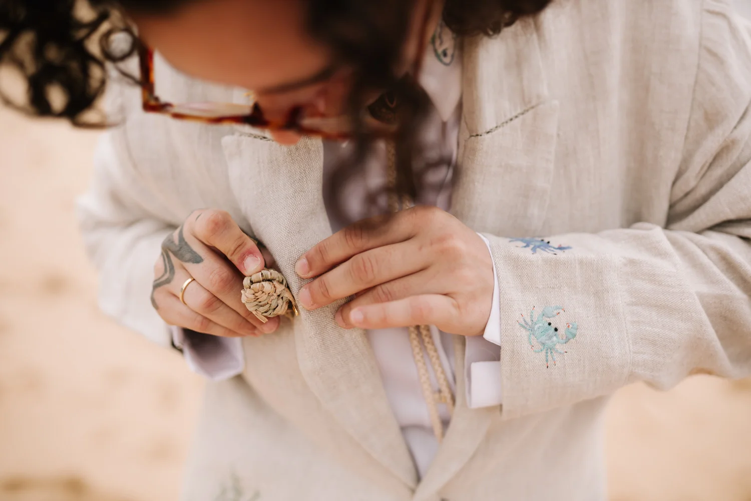 A person in a linen blazer with crab embroidery holds a woven boutonniere at Pouso das Flores in Paraty, Brazil.