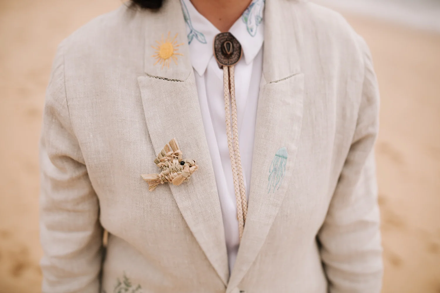 Close-up of a linen blazer with ocean embroidery, raffia fish boutonniere, and bolo tie at Pouso das Flores in Paraty.