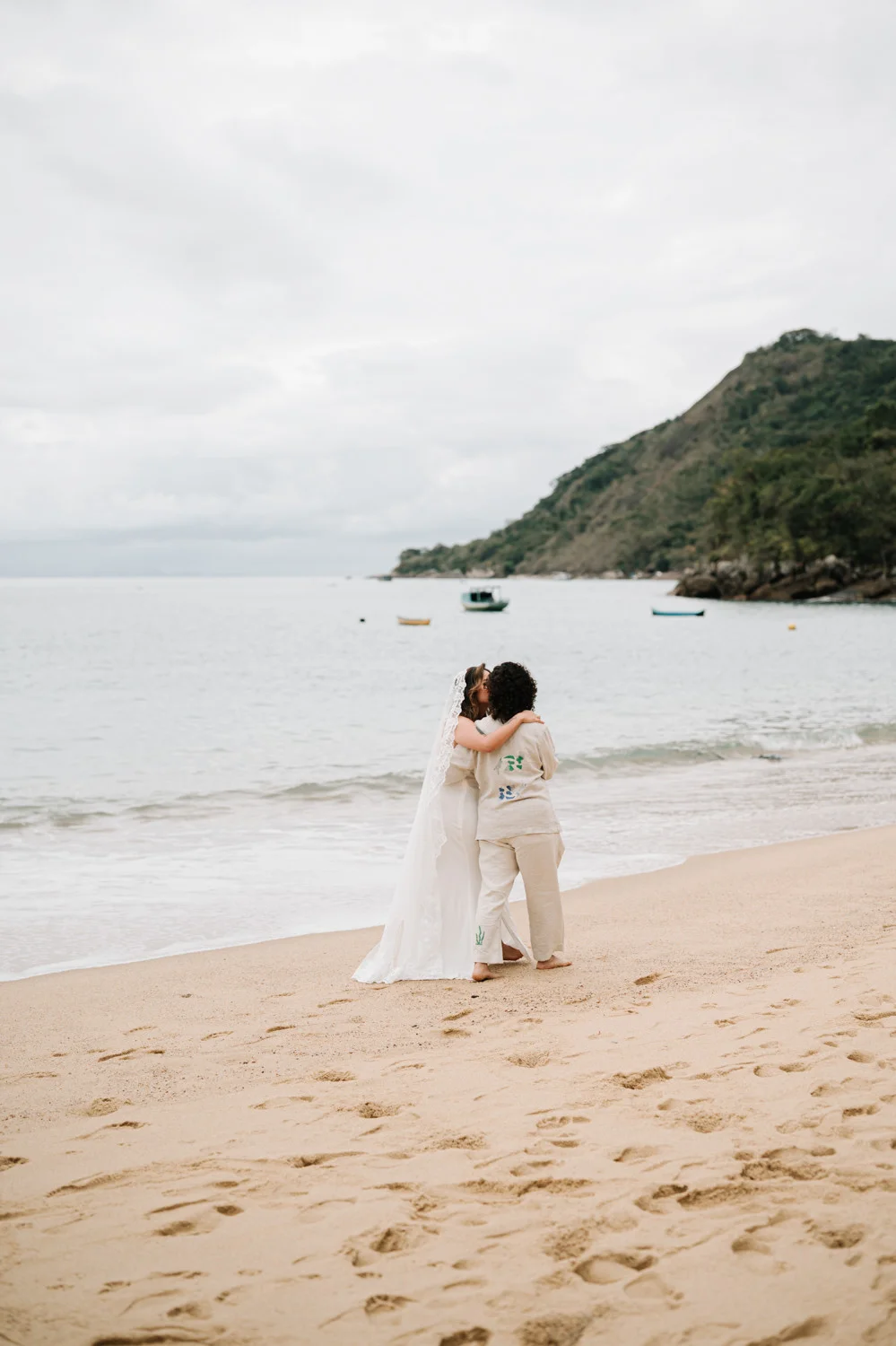 Rafaela and Nathalia kiss barefoot on the beach at Pouso das Flores in Paraty, Brazil.