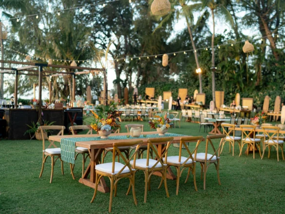 Wide view of the beach house lawn at the Engage!26 Maui Aloha welcome party showing farm tables with teal runners, tropical floral centerpieces, crossback chairs and string lights at Ritz-Carlton Kapalua