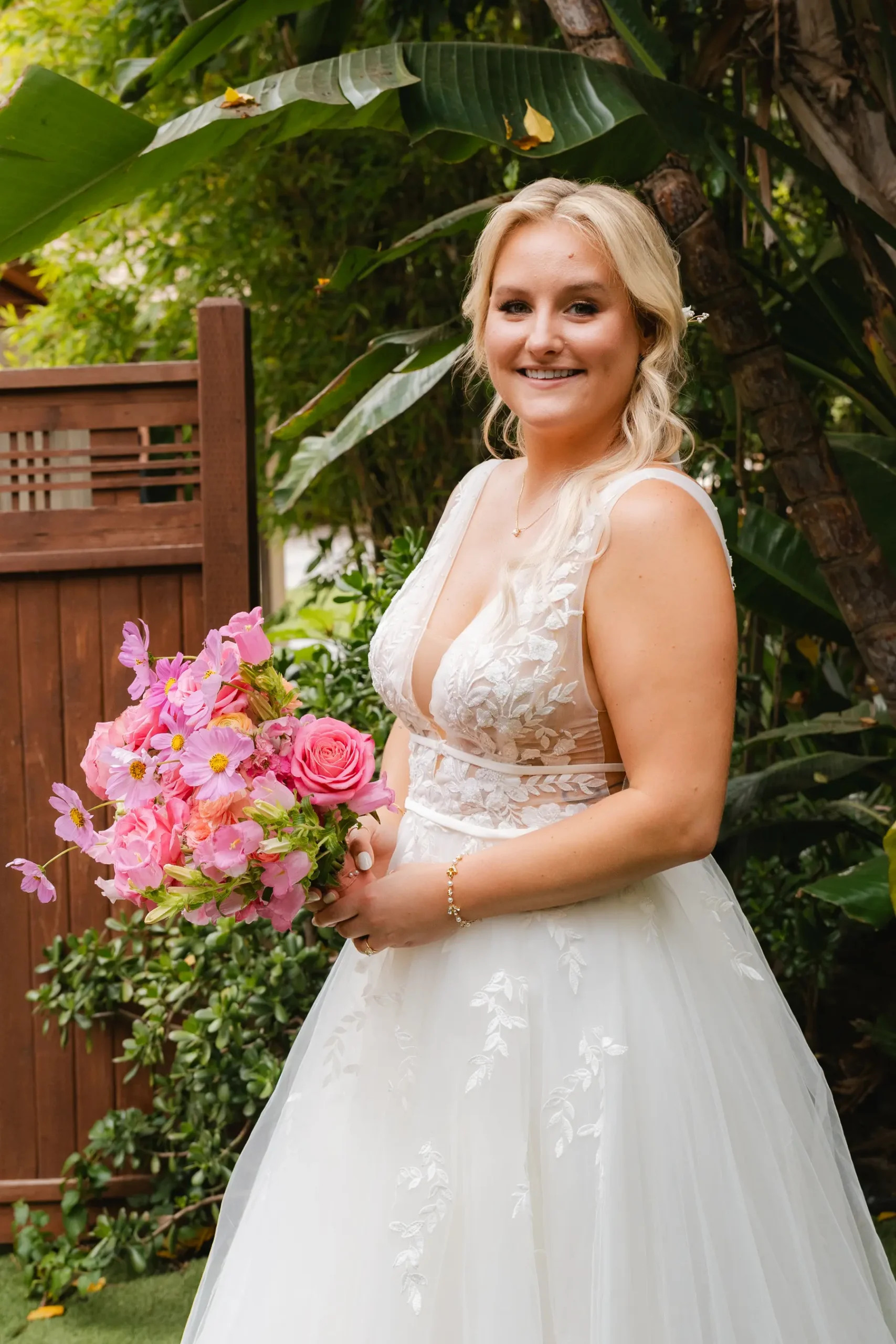 Bride smiles holding a pink bouquet in a lace wedding gown at Botanica in Oceanside, California.
