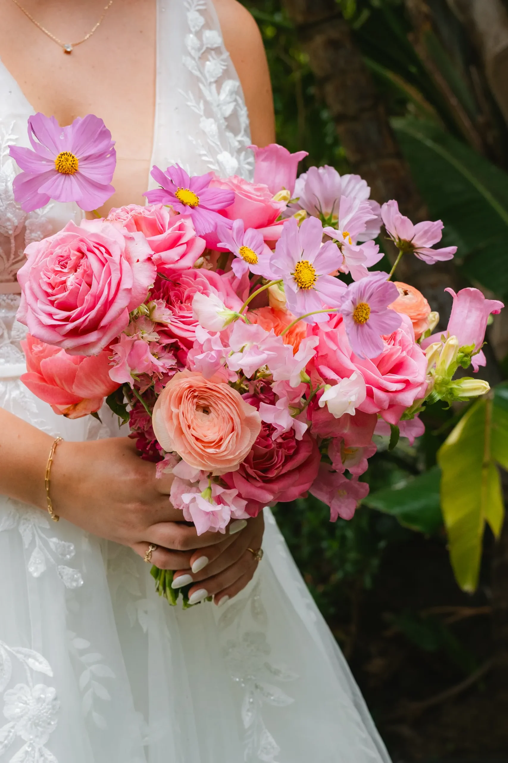 Bride holds a lush pink bridal bouquet of roses, ranunculus and cosmos at Botanica in Oceanside, California.