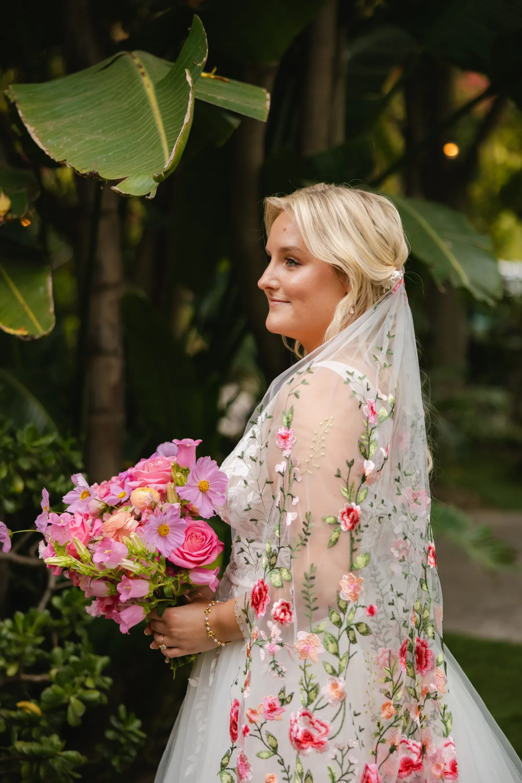 Bride in a floral embroidered gown and matching veil holds a pink bouquet at Botanica in Oceanside, California.