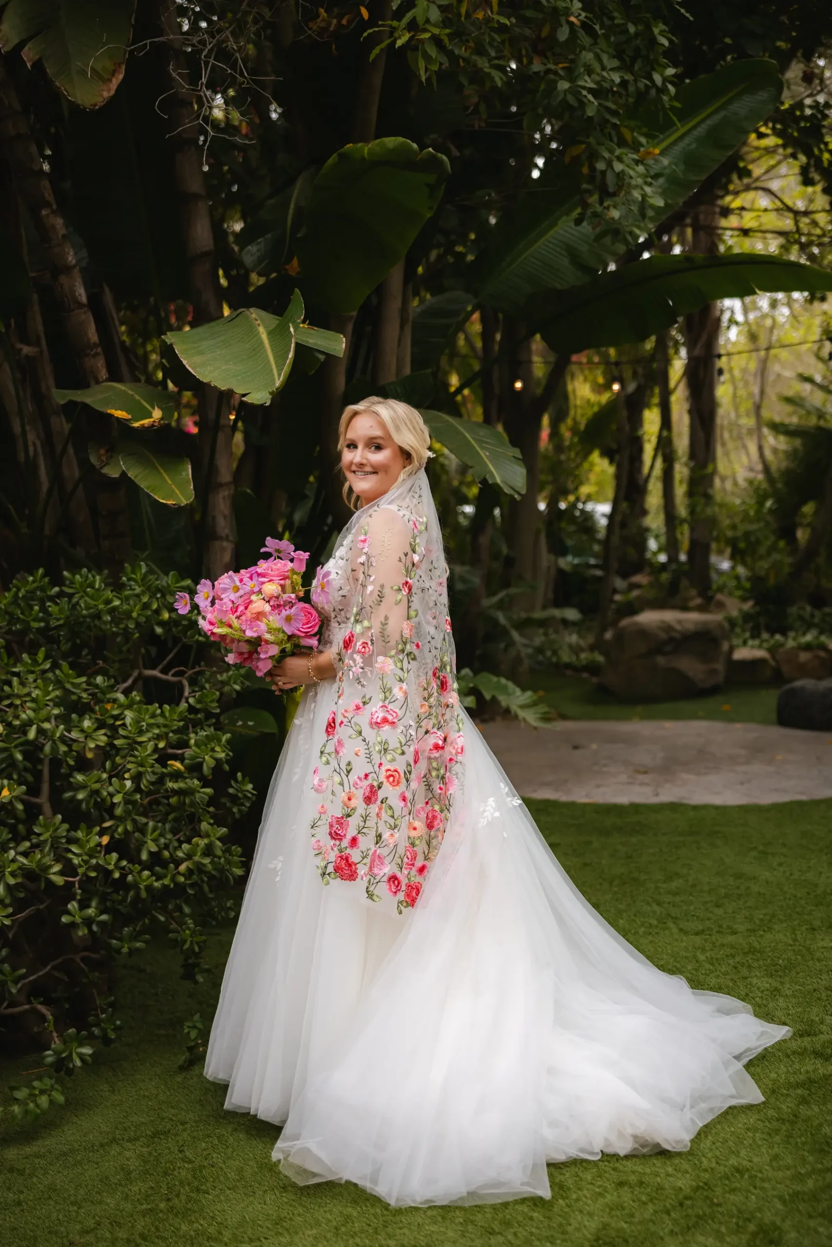 Bride in a floral-embroidered white gown holds a pink bouquet at Botanica in Oceanside, California.