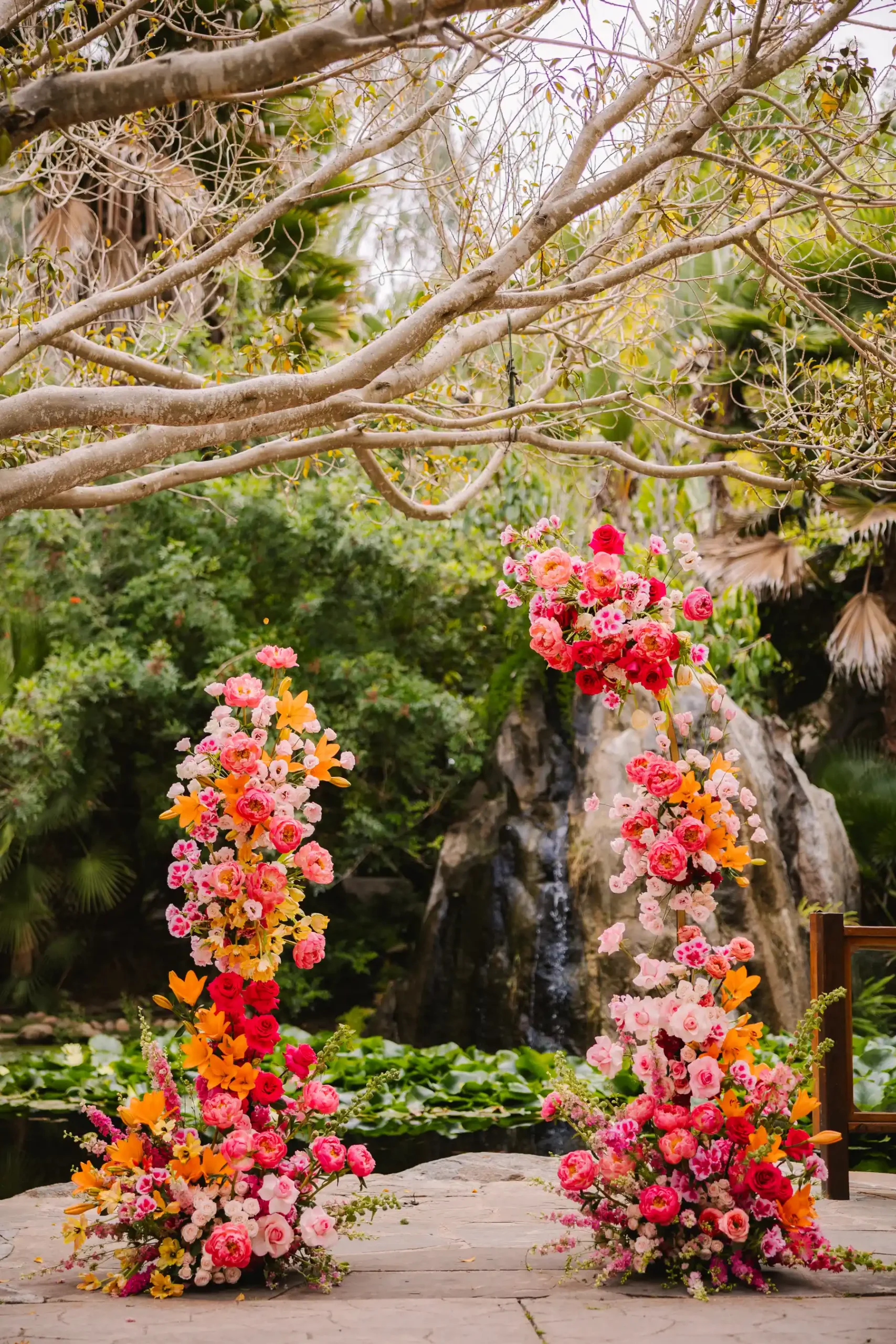 Vibrant floral ceremony arches with pink, red and orange blooms at Botanica in Oceanside, California.