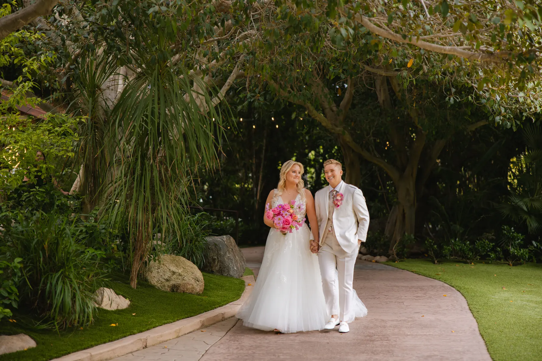Erika Beursken and Melissa Brodsky walk hand in hand through lush garden path at Botanica in Oceanside, California.
