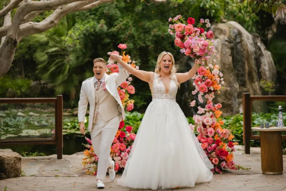 Erika Beursken and Melissa Brodsky celebrate after their ceremony at Botanica in Oceanside, California, surrounded by vibrant floral arches.