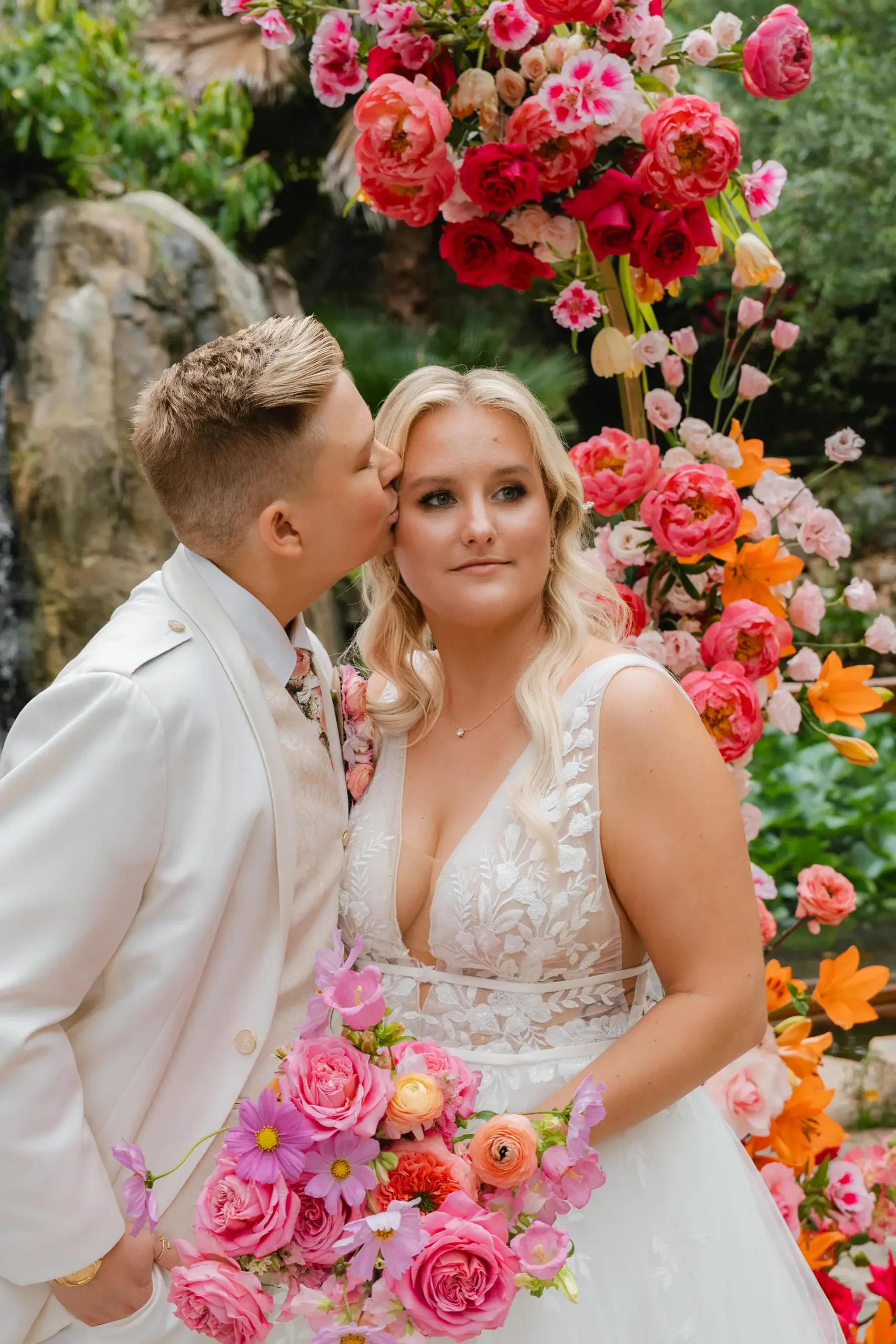 Erika Beursken and Melissa Brodsky pose before a vibrant floral arch at Botanica in Oceanside, California.