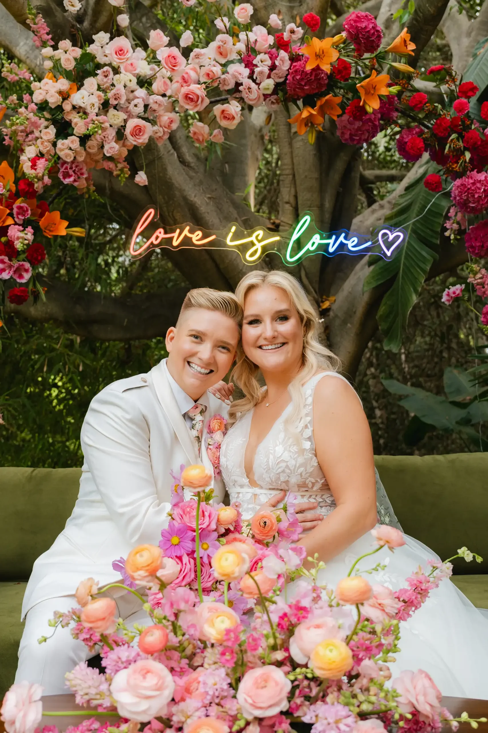 Erika Beursken and Melissa Brodsky smile together beneath a rainbow 'love is love' neon sign at Botanica in Oceanside, California.