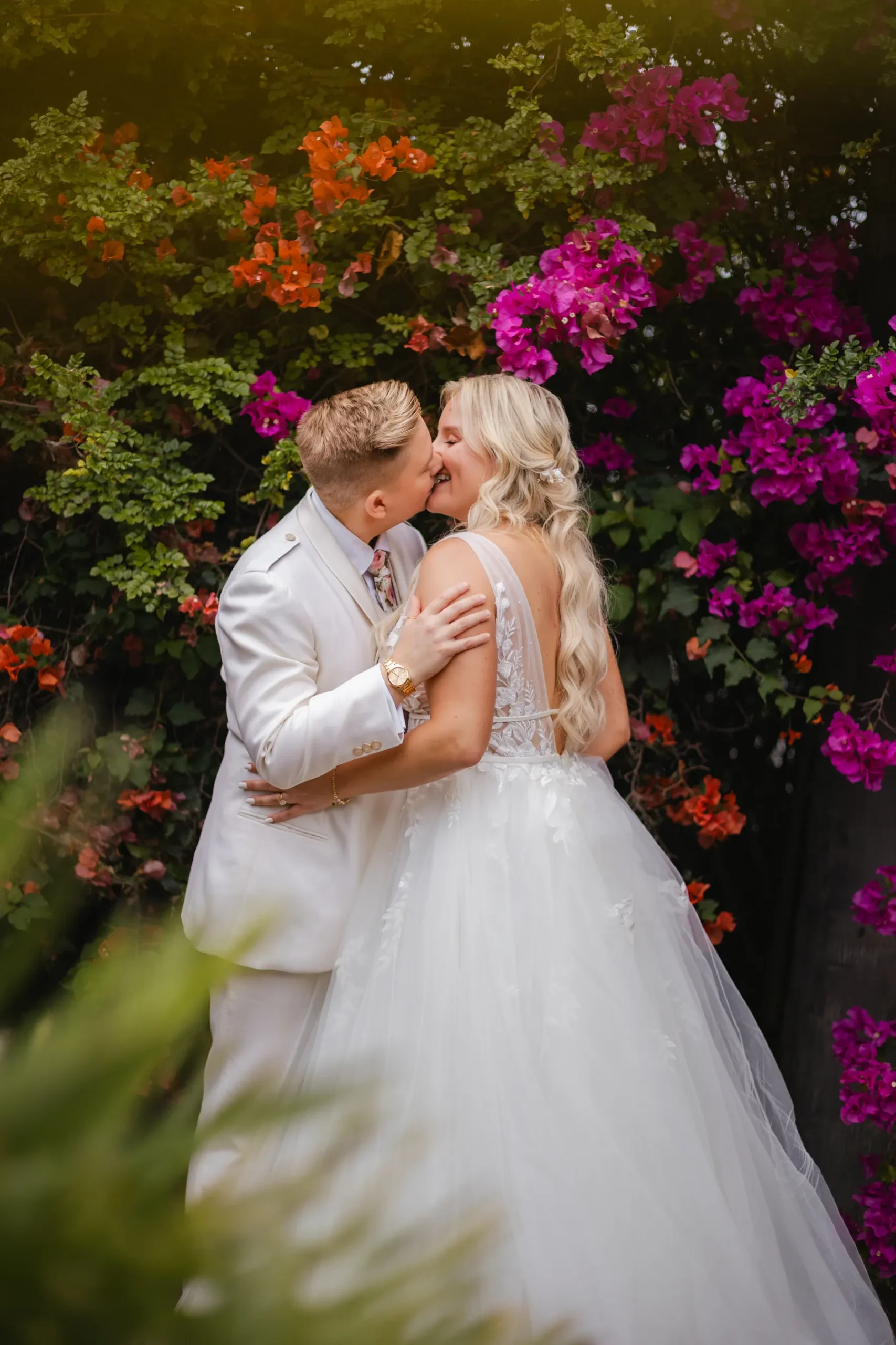 Erika Beursken and Melissa Brodsky share a kiss surrounded by vibrant bougainvillea at Botanica in Oceanside, California.