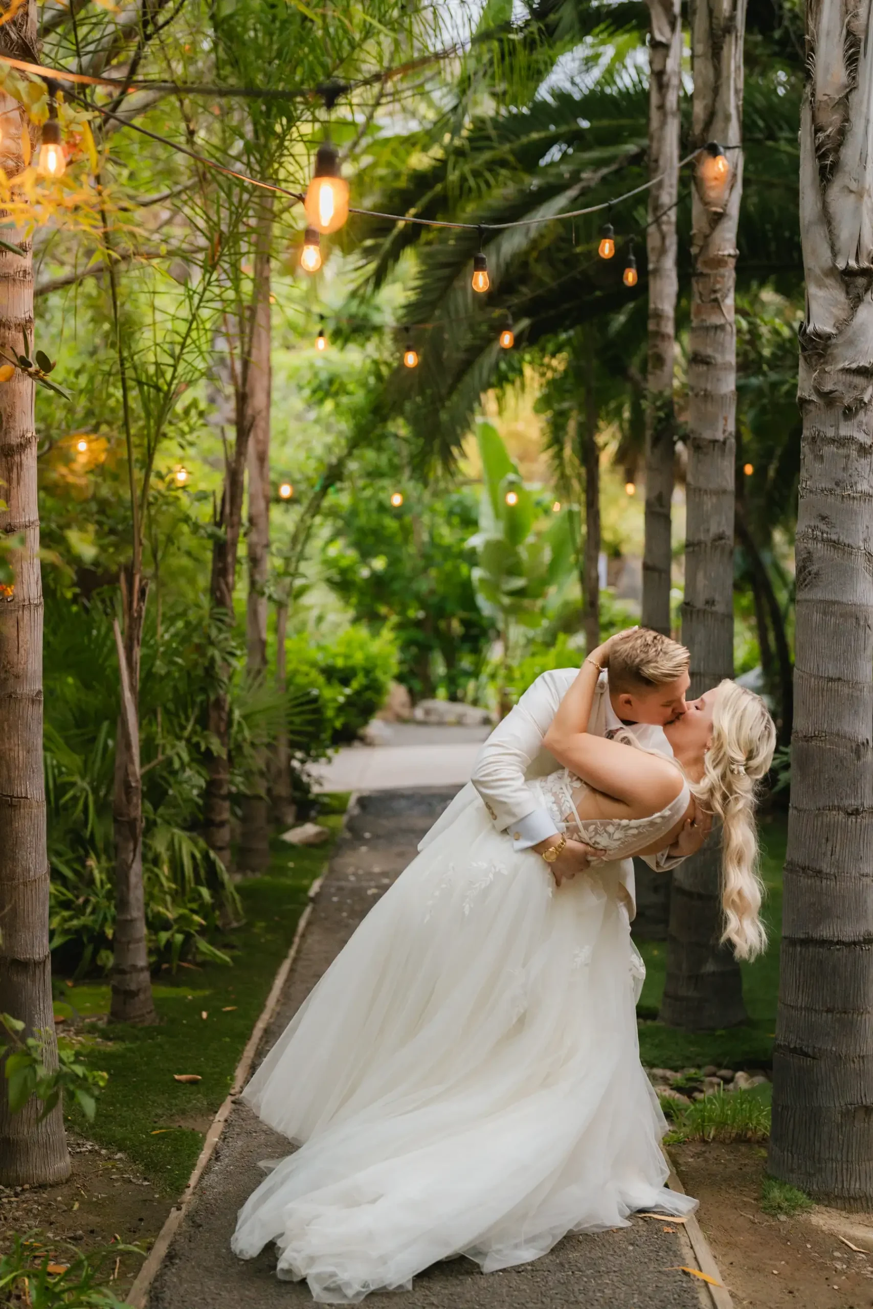Erika Beursken and Melissa Brodsky share a dip kiss along a palm-lined path at Botanica in Oceanside, California.