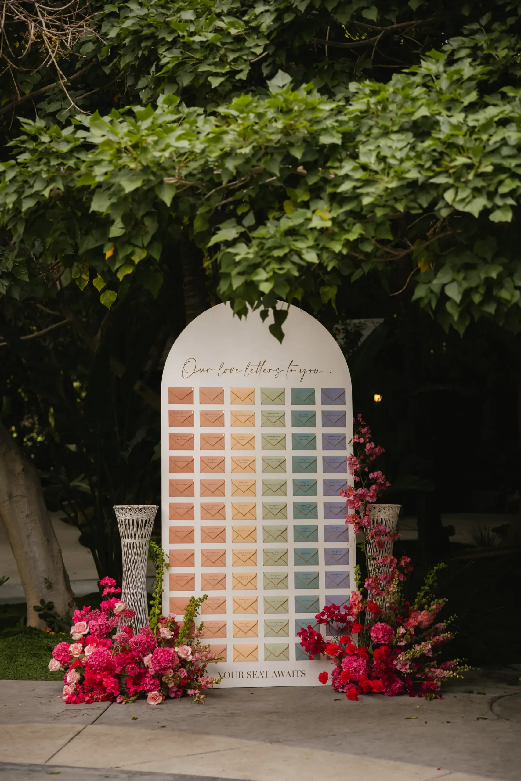 Rainbow envelope seating chart display reading 'Our Love Letters to You' at lesbian garden wedding at Botanica in Oceanside, California.