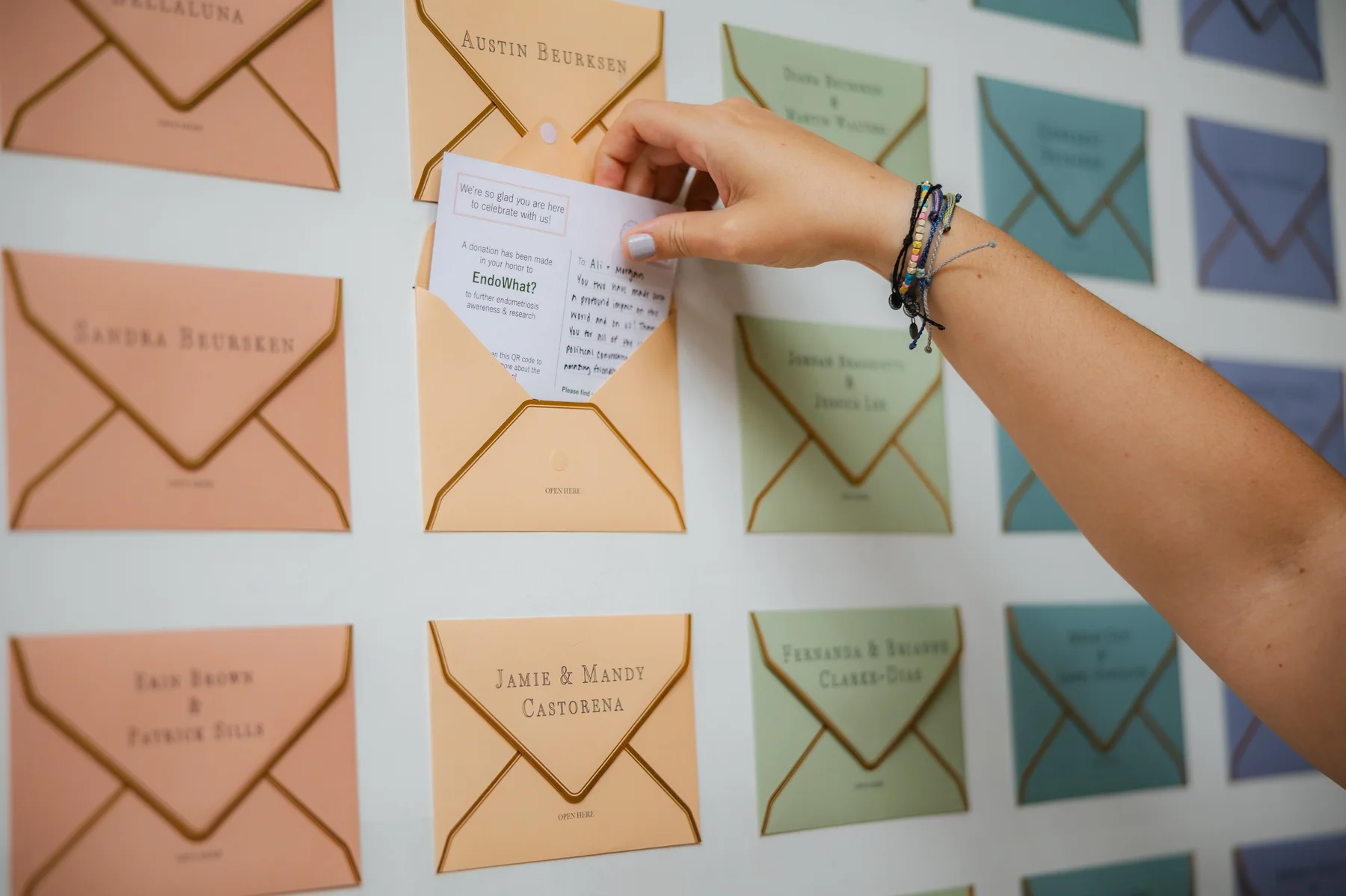 A guest pulls a seating card from an envelope wall at Erika Beursken and Melissa Brodsky's wedding at Botanica in Oceanside, California.