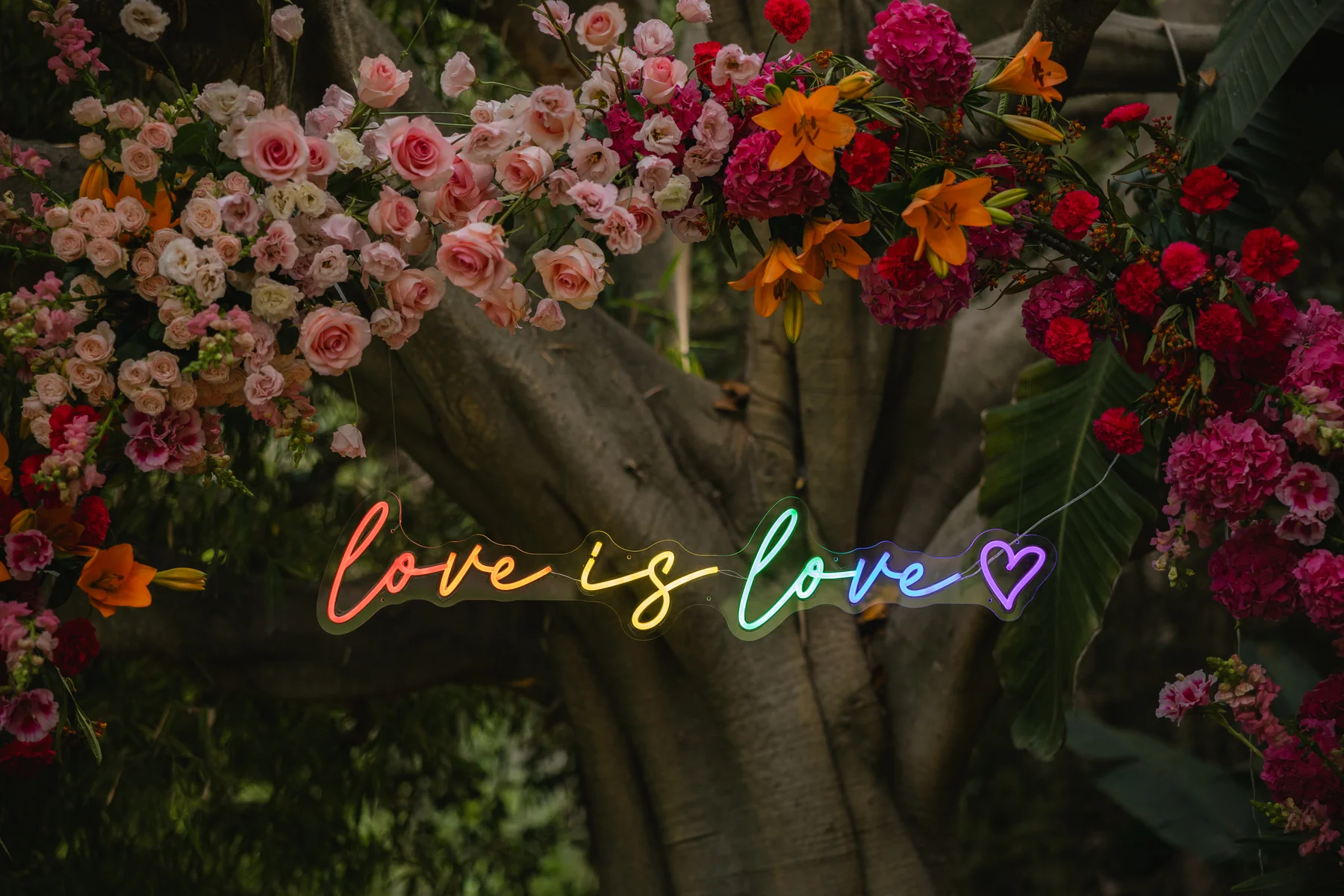 Rainbow neon 'love is love' sign glows among lush floral arrangements of pink roses and orange lilies at Botanica in Oceanside, California.
