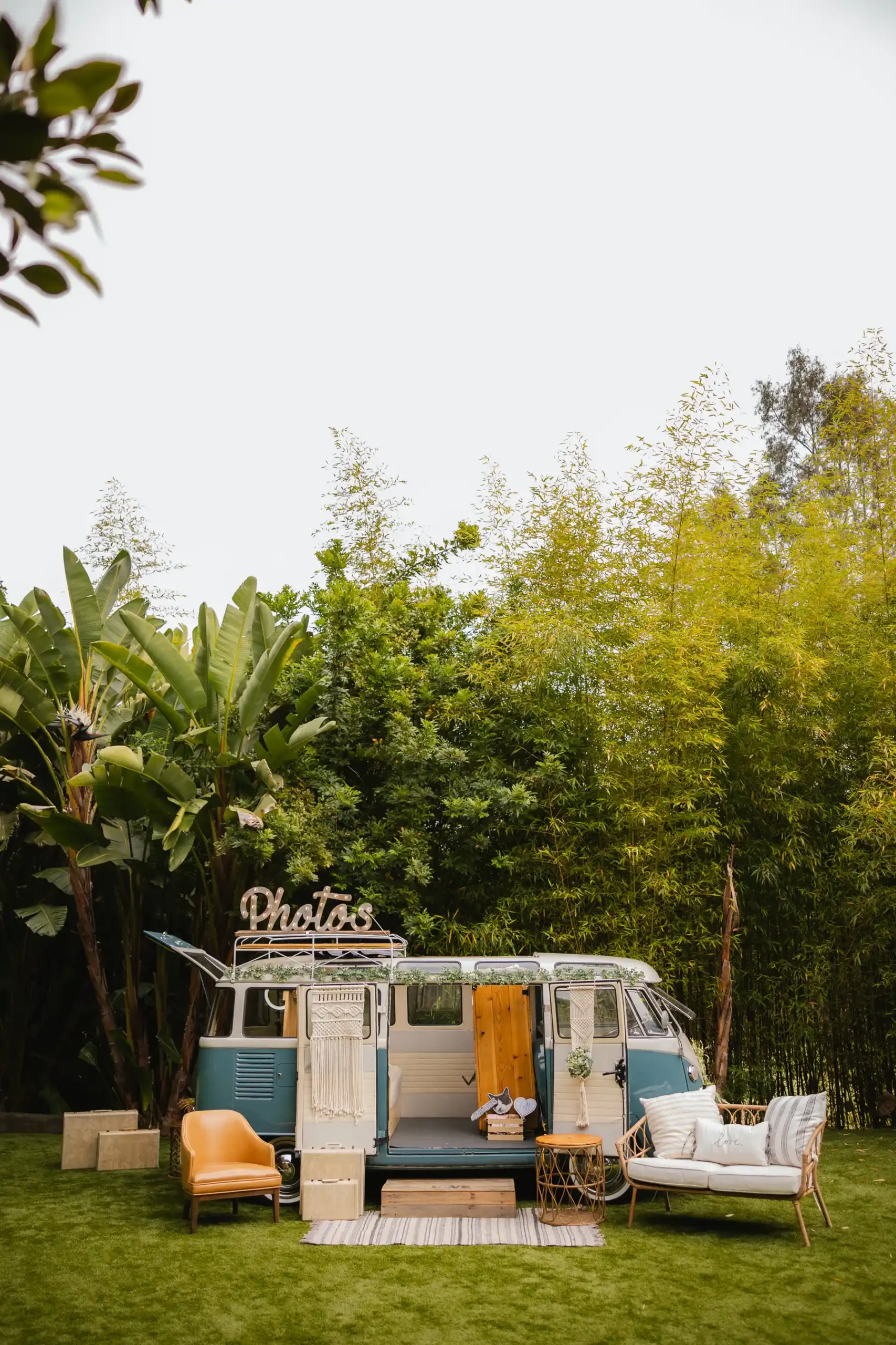 A vintage teal VW bus photo booth with macrame decor and a 'Photos' sign at Botanica in Oceanside, California.