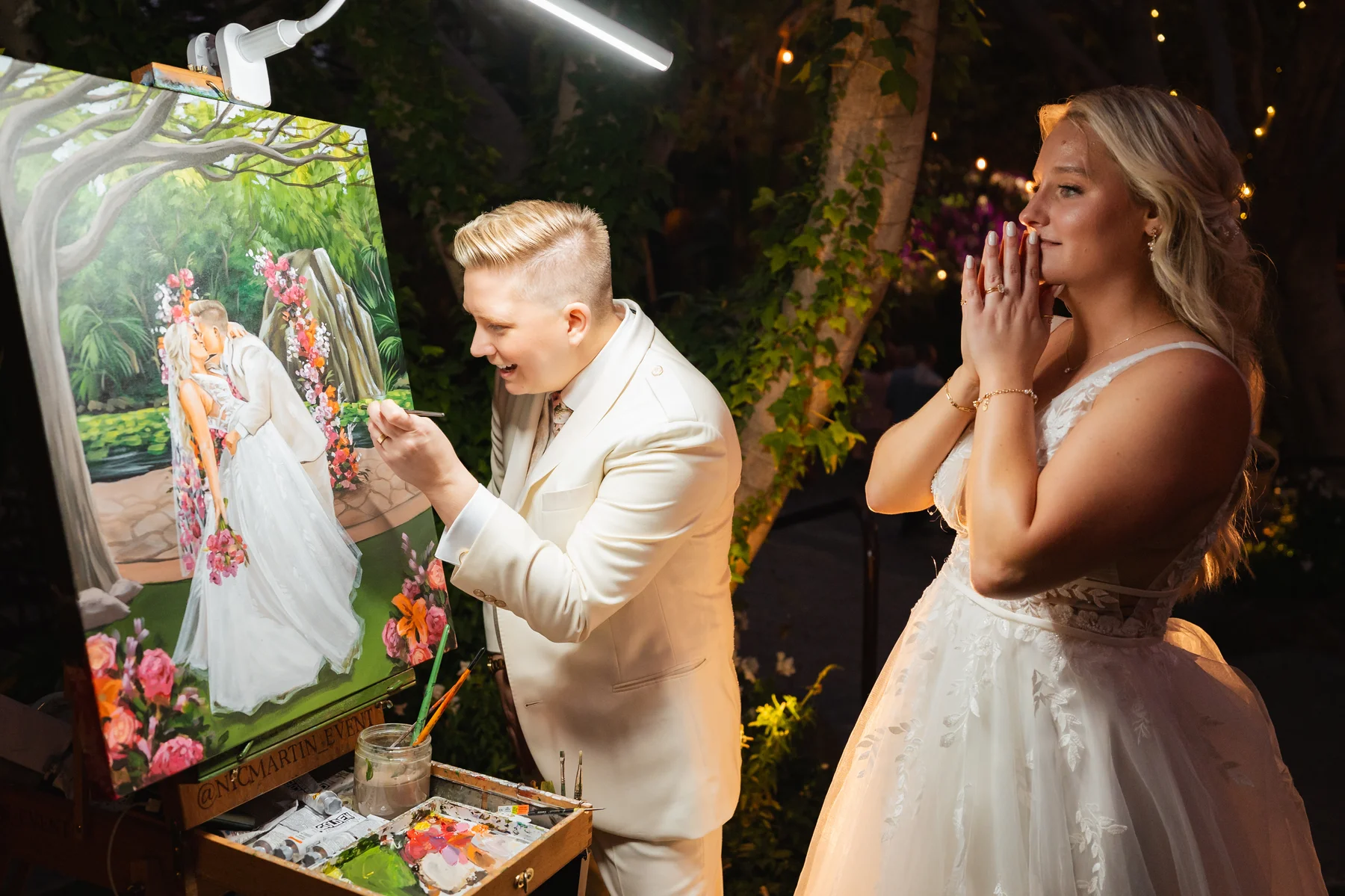 A live wedding painter adds finishing touches to a portrait of Erika and Melissa at Botanica in Oceanside, California, as the bride looks on in awe.