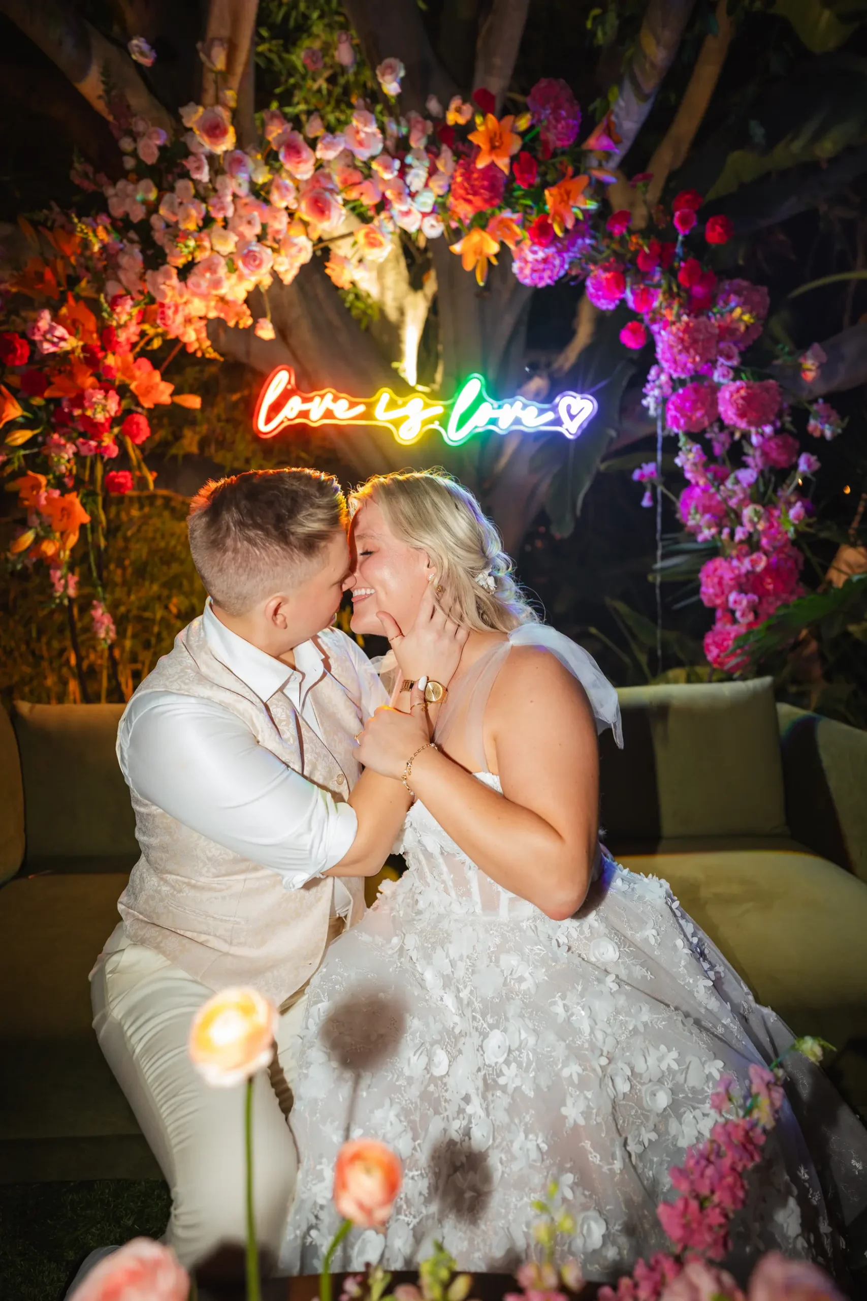 Erika Beursken and Melissa Brodsky share a joyful moment beneath a rainbow 'love is love' neon sign at Botanica in Oceanside, California.