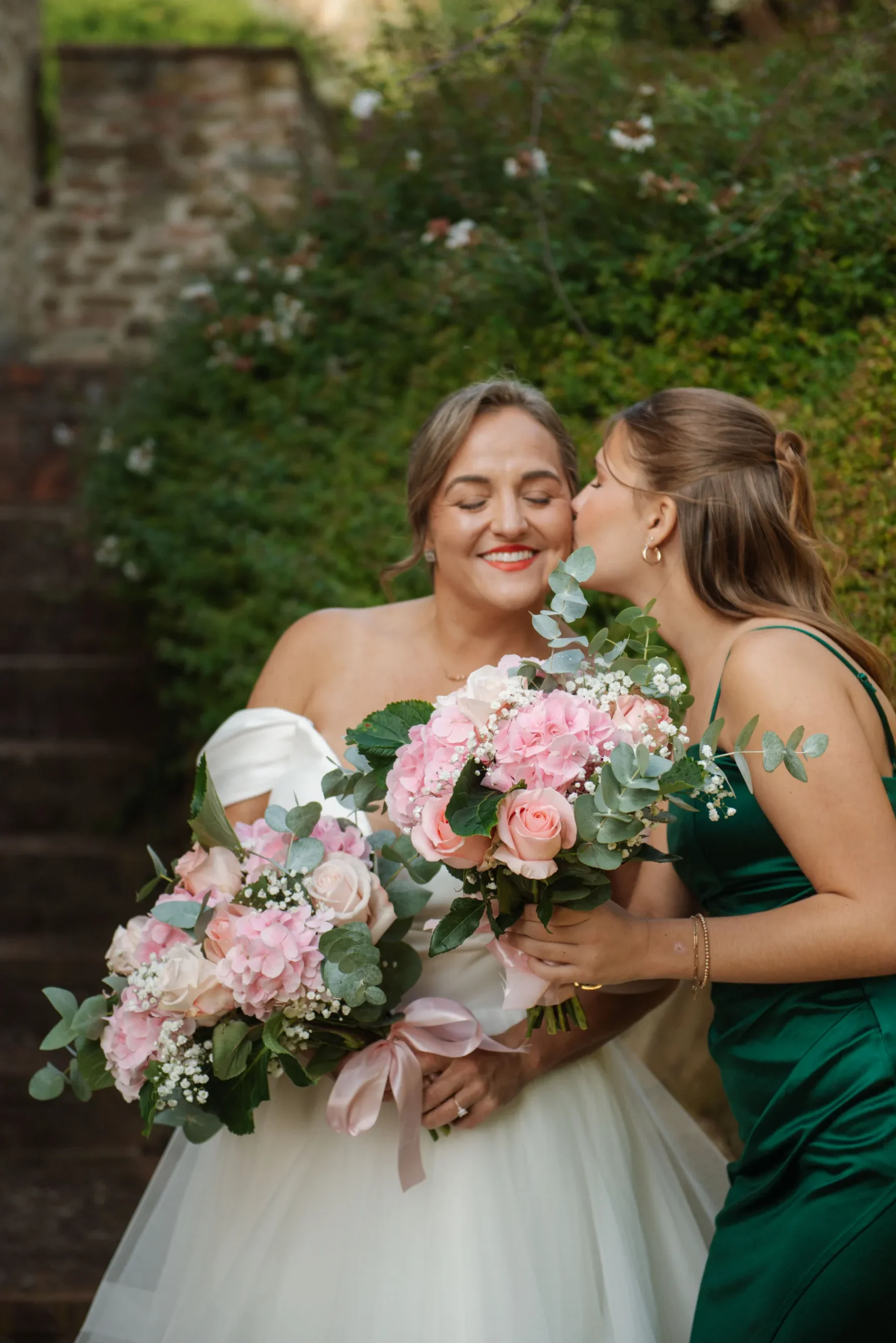 Bride Lauren Thomas smiles as bridesmaid kisses her cheek, both holding pink bouquets at Casa Cornacchi in Tuscany.