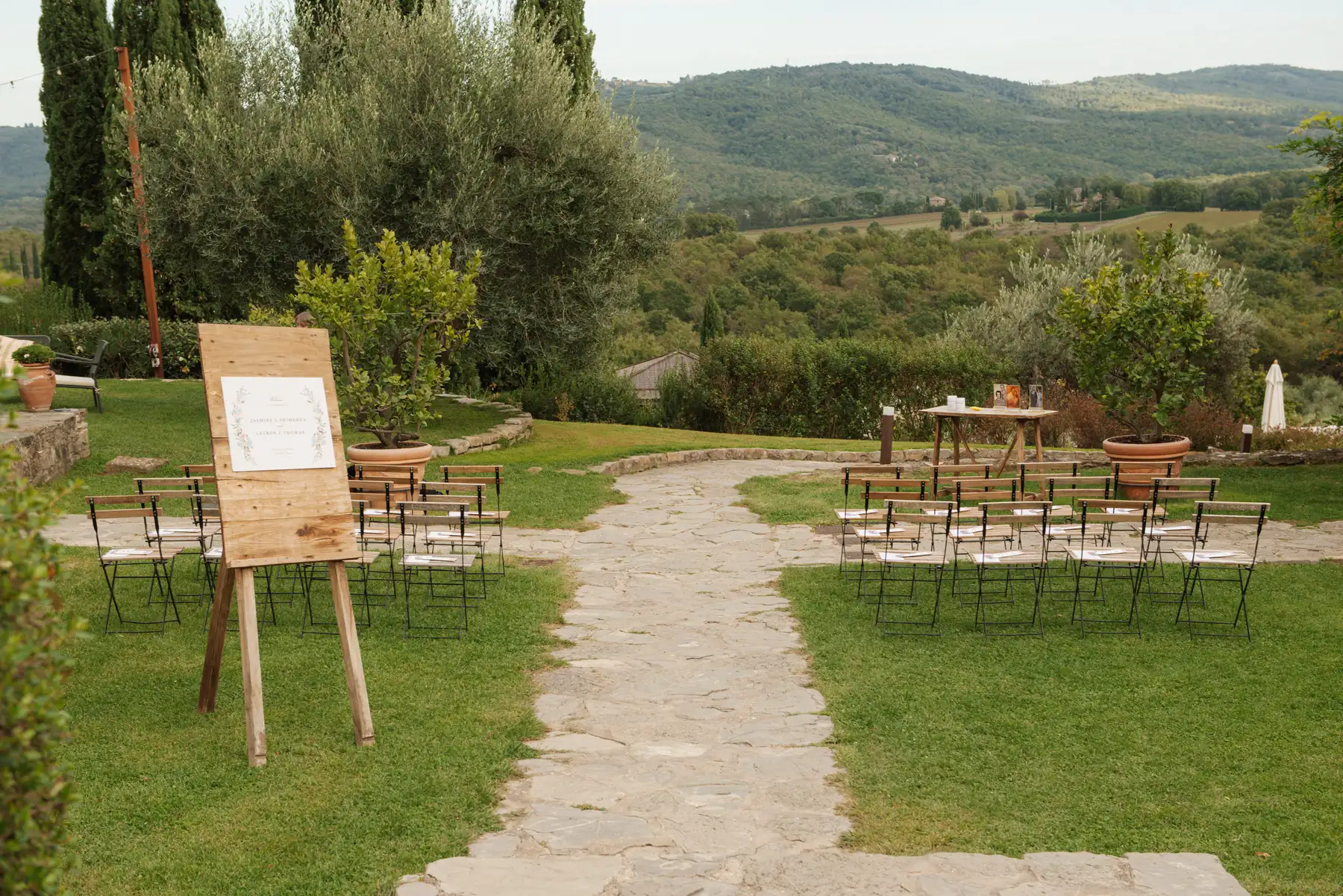 Outdoor ceremony setup at Casa Cornacchi in Tuscany with chairs, stone path, and wooden welcome sign for Lauren Thomas and Jasmine Shimerda.