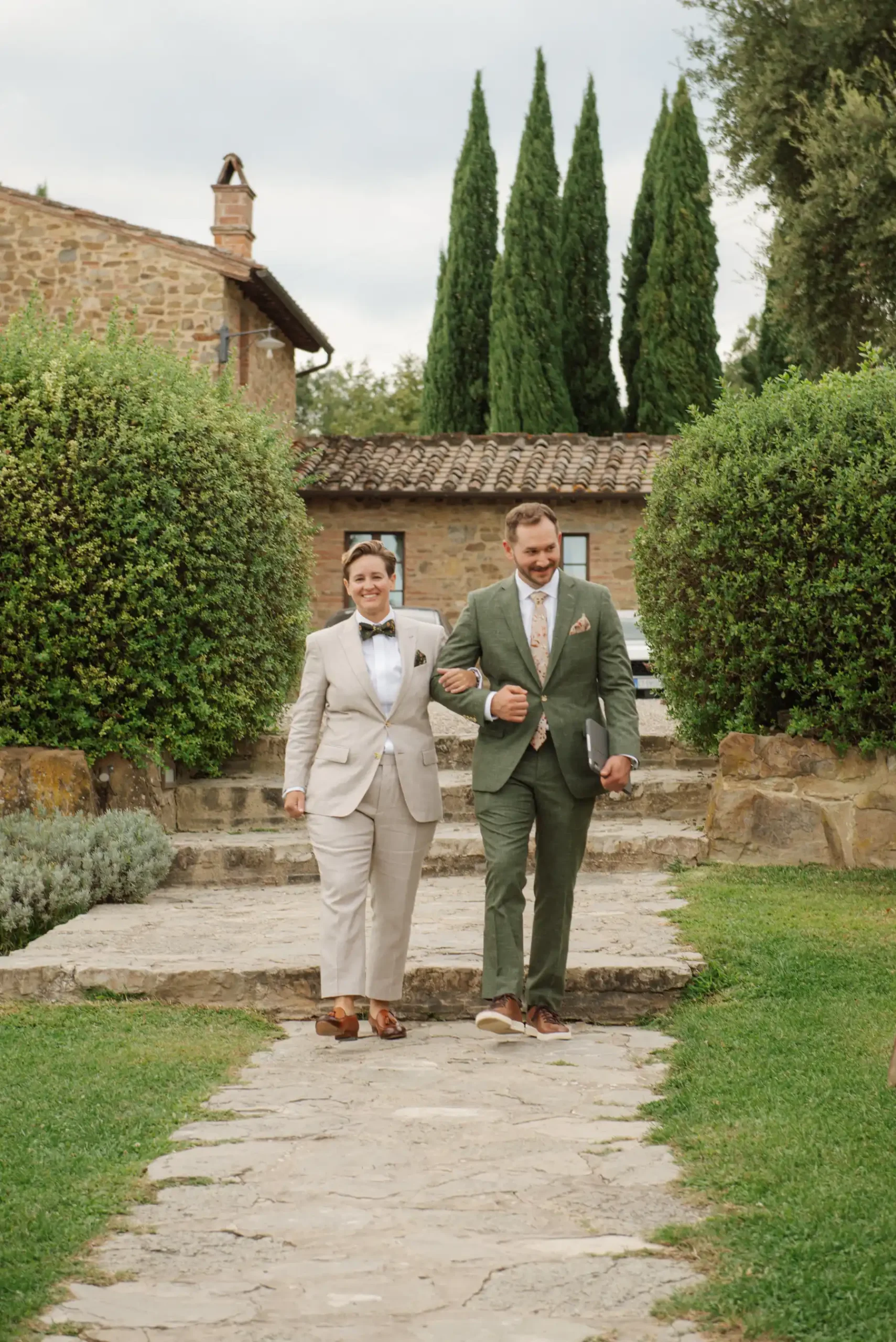 Lauren Thomas and Jasmine Shimerda walk arm-in-arm along a stone path at Casa Cornacchi in Tuscany, Italy.