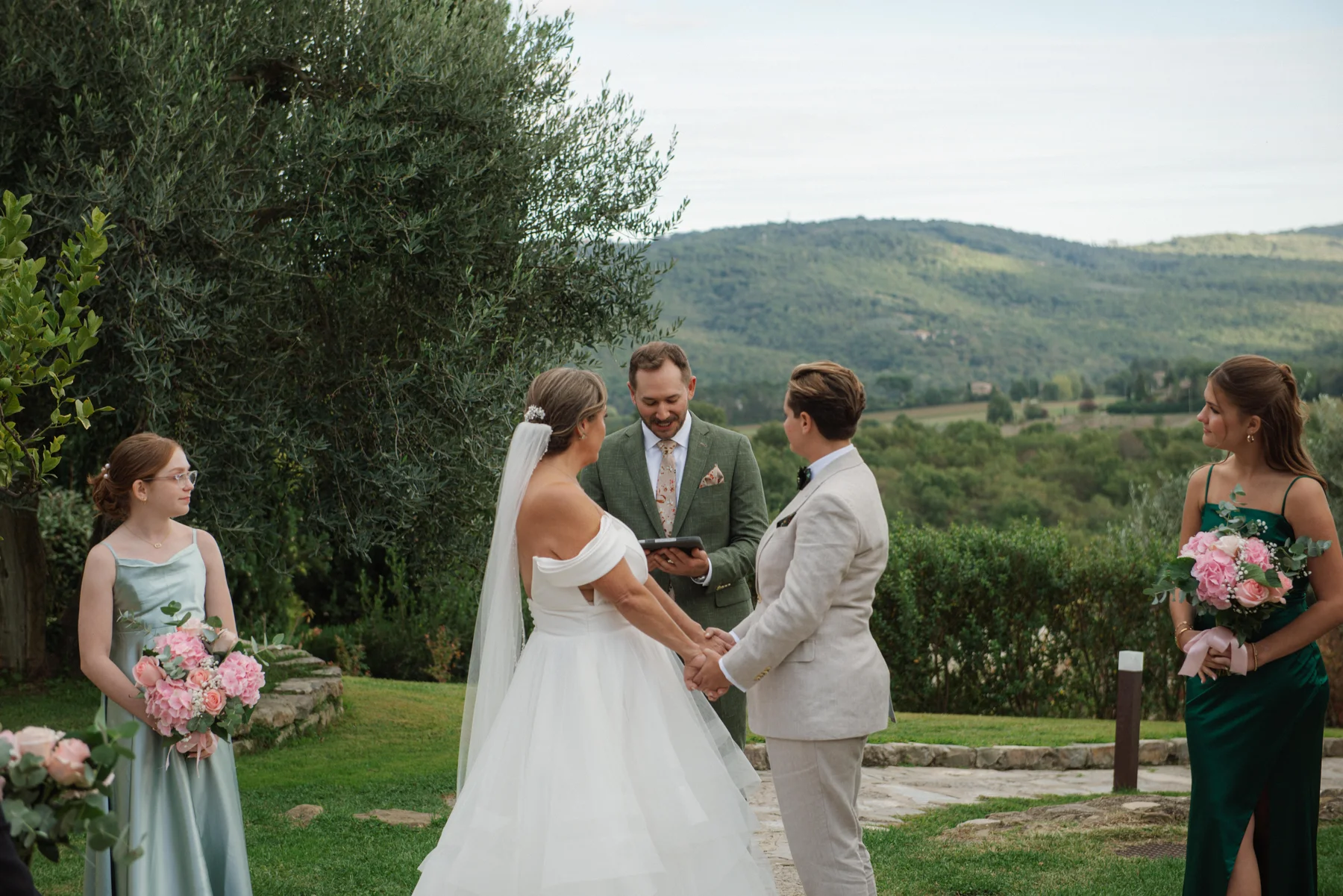 Lauren Thomas and Jasmine Shimerda exchange vows at Casa Cornacchi in Arezzo, Tuscany, with rolling hills behind them.