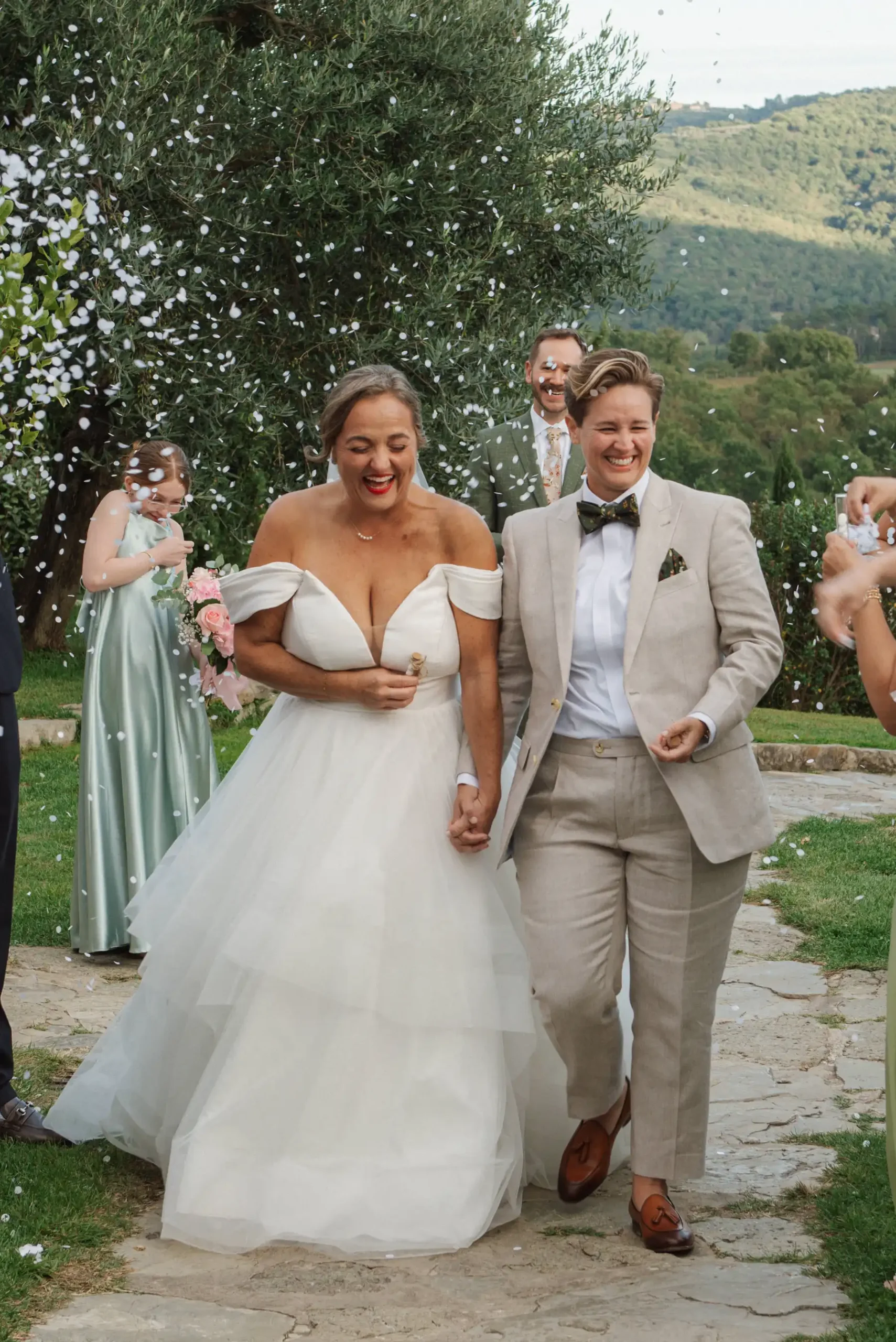 Lauren Thomas and Jasmine Shimerda walk hand in hand through a confetti shower after their wedding ceremony at Casa Cornacchi in Tuscany.