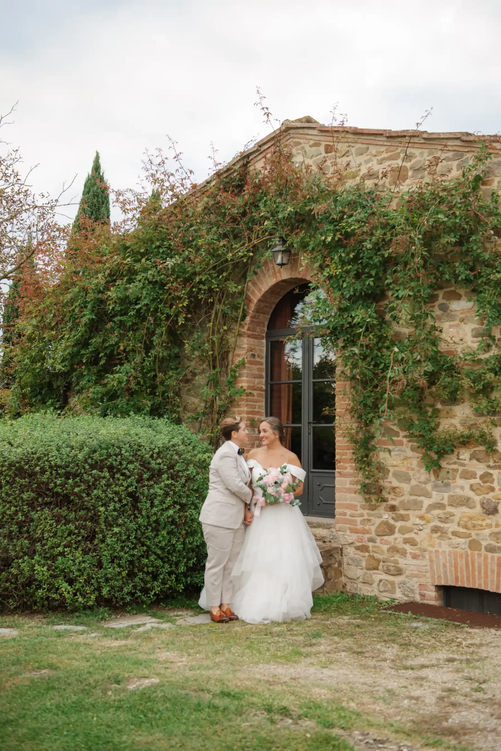 Lauren Thomas and Jasmine Shimerda share a tender moment outside the ivy-covered stone walls of Casa Cornacchi in Tuscany.