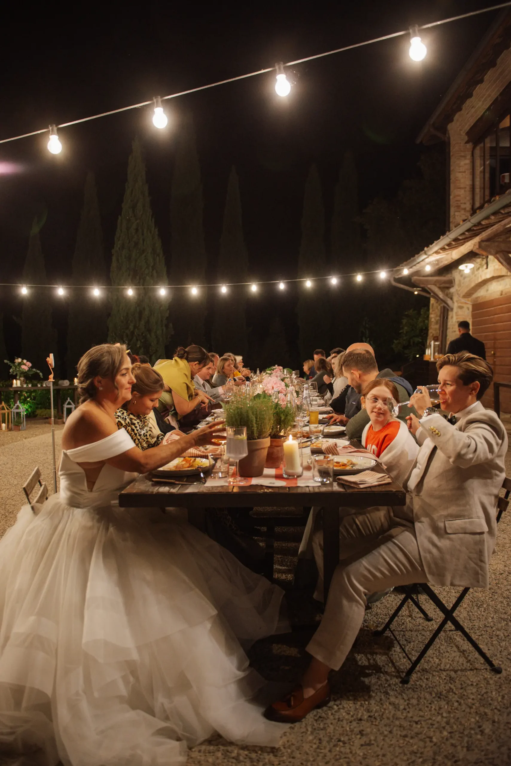 Lauren Thomas and Jasmine Shimerda dine with guests at a long outdoor table under string lights at Casa Cornacchi in Tuscany.