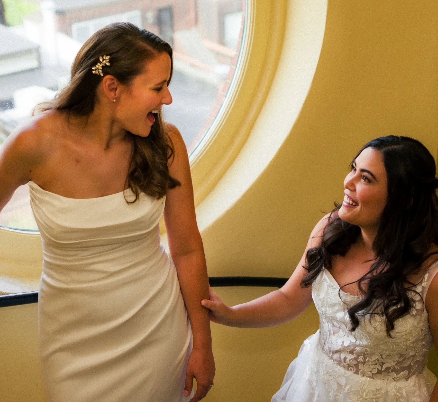 Brides Ashton Hattori and Stephanie Tillman share a joyful moment in white wedding gowns at Hampshire House in Boston.