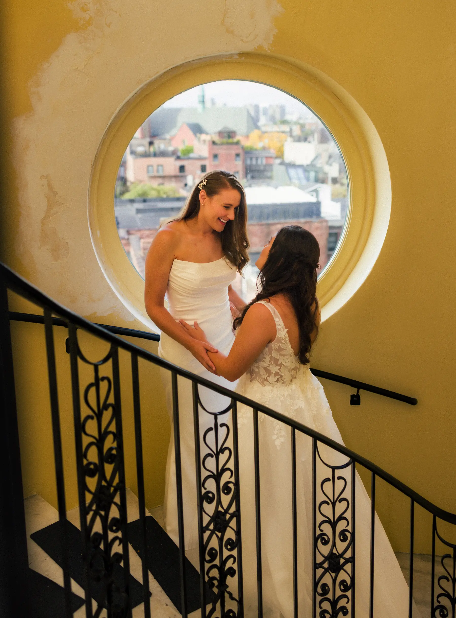 Brides Ashton Hattori and Stephanie Tillman hold hands and smile at each other on a spiral staircase at Hampshire House in Boston.