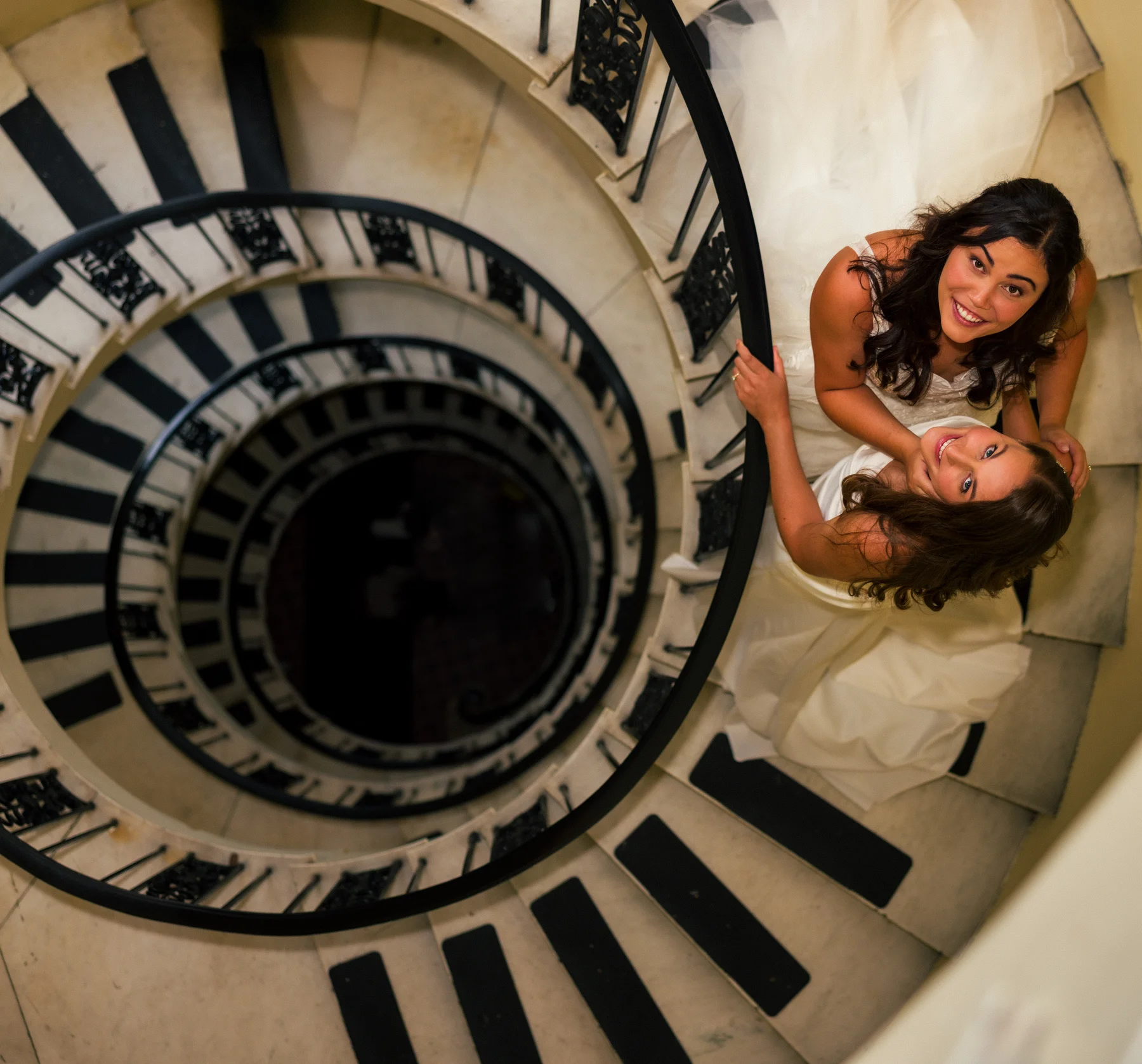 Ashton Hattori and Stephanie Tillman in white gowns smile up from a spiral staircase at Hampshire House in Boston.