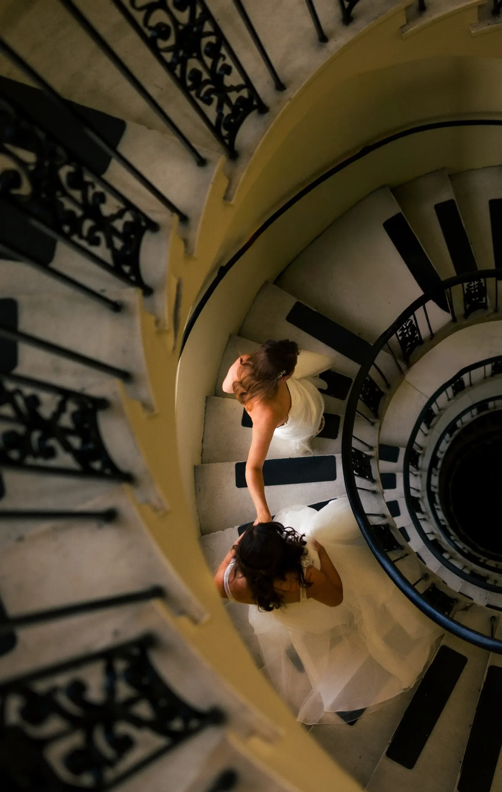 Brides Ashton Hattori and Stephanie Tillman in white gowns on a spiral staircase at Hampshire House in Boston.
