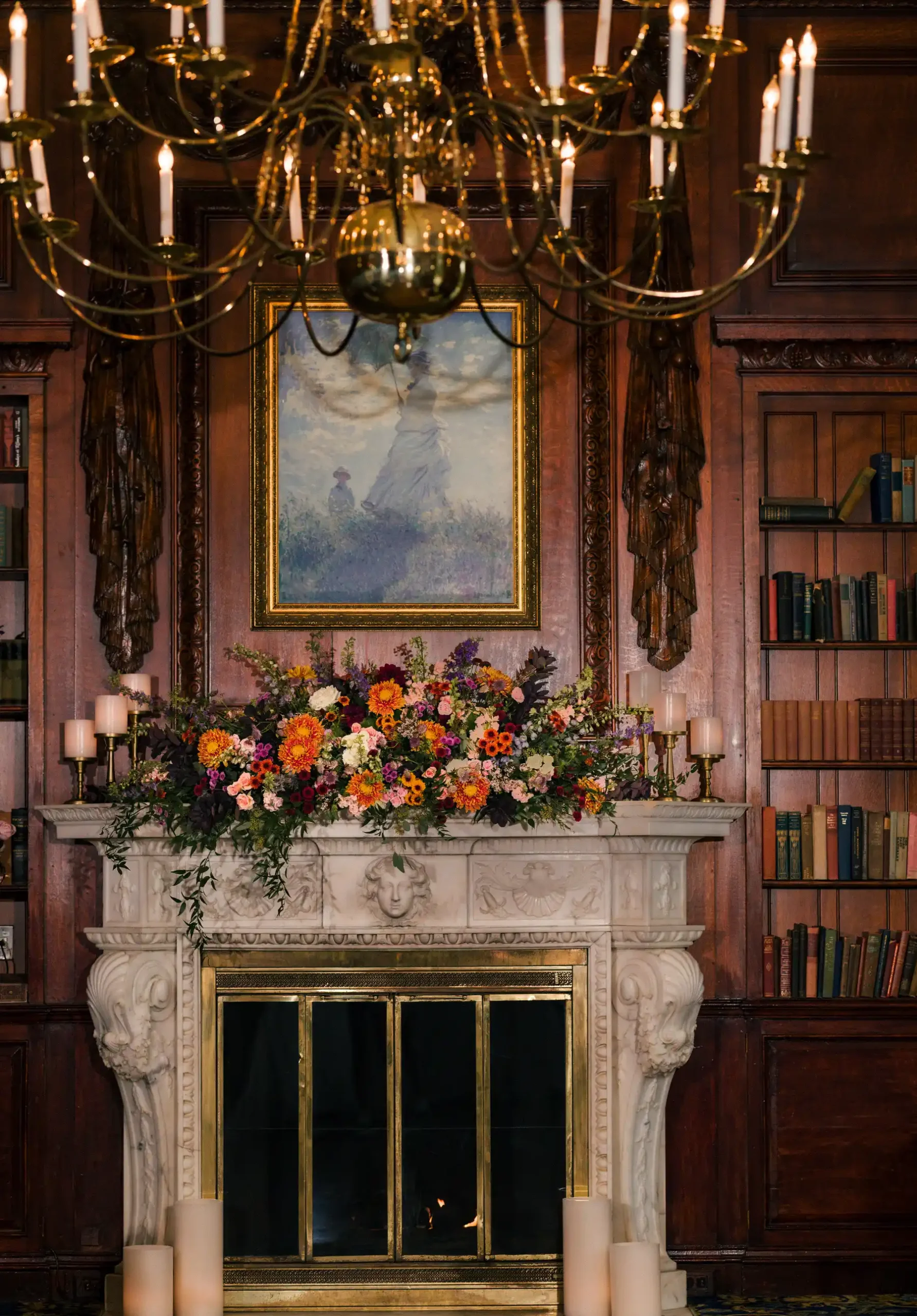 Ornate marble fireplace at Hampshire House adorned with vibrant fall floral arrangement beneath a Monet-style painting and brass chandelier.