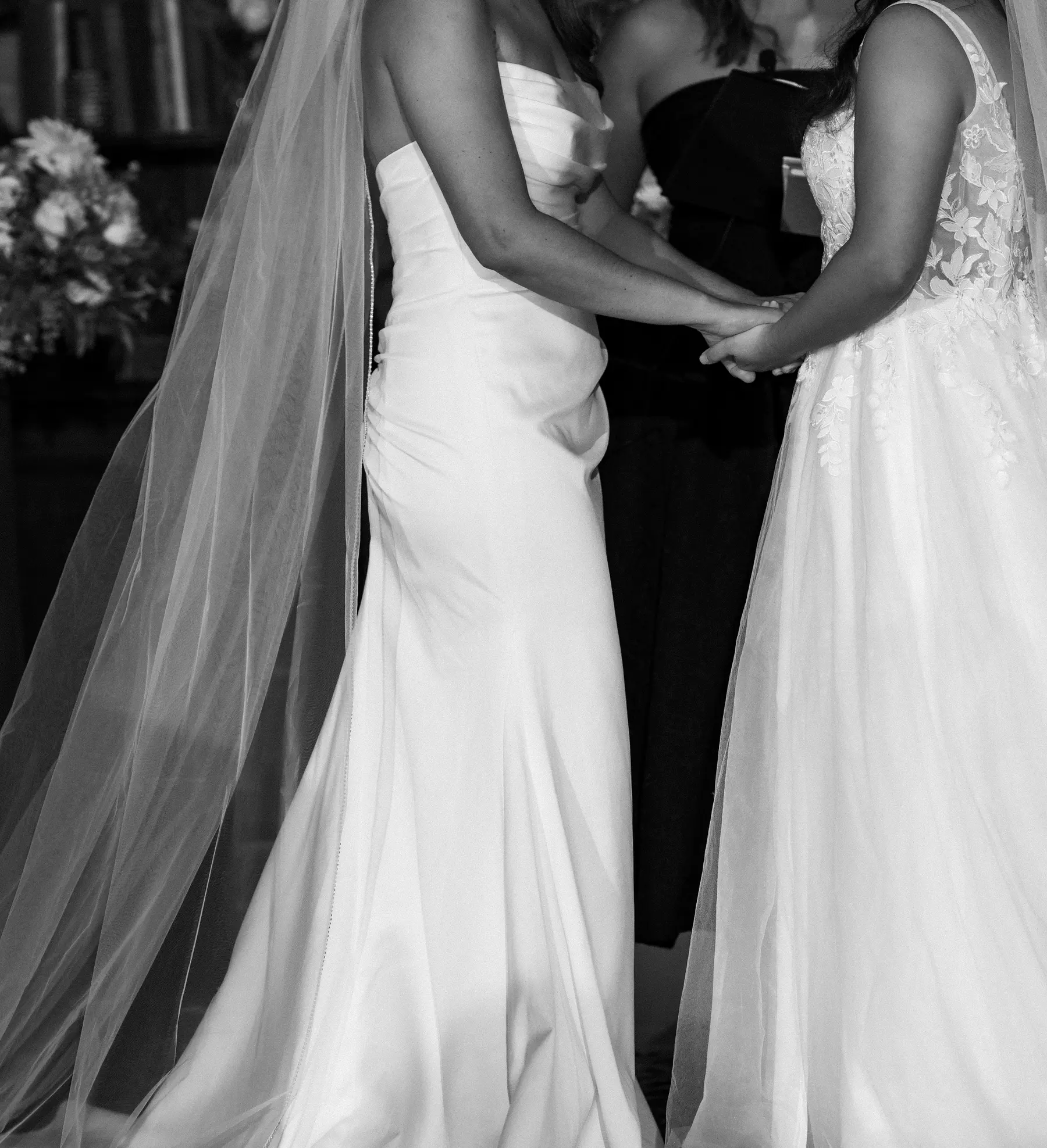 Brides Ashton Hattori and Stephanie Tillman hold hands in white gowns during their ceremony at Hampshire House in Boston.