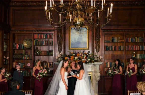 Ashton Hattori and Stephanie Tillman exchange vows before an ornate fireplace at Hampshire House in Boston, surrounded by bridesmaids in burgundy.