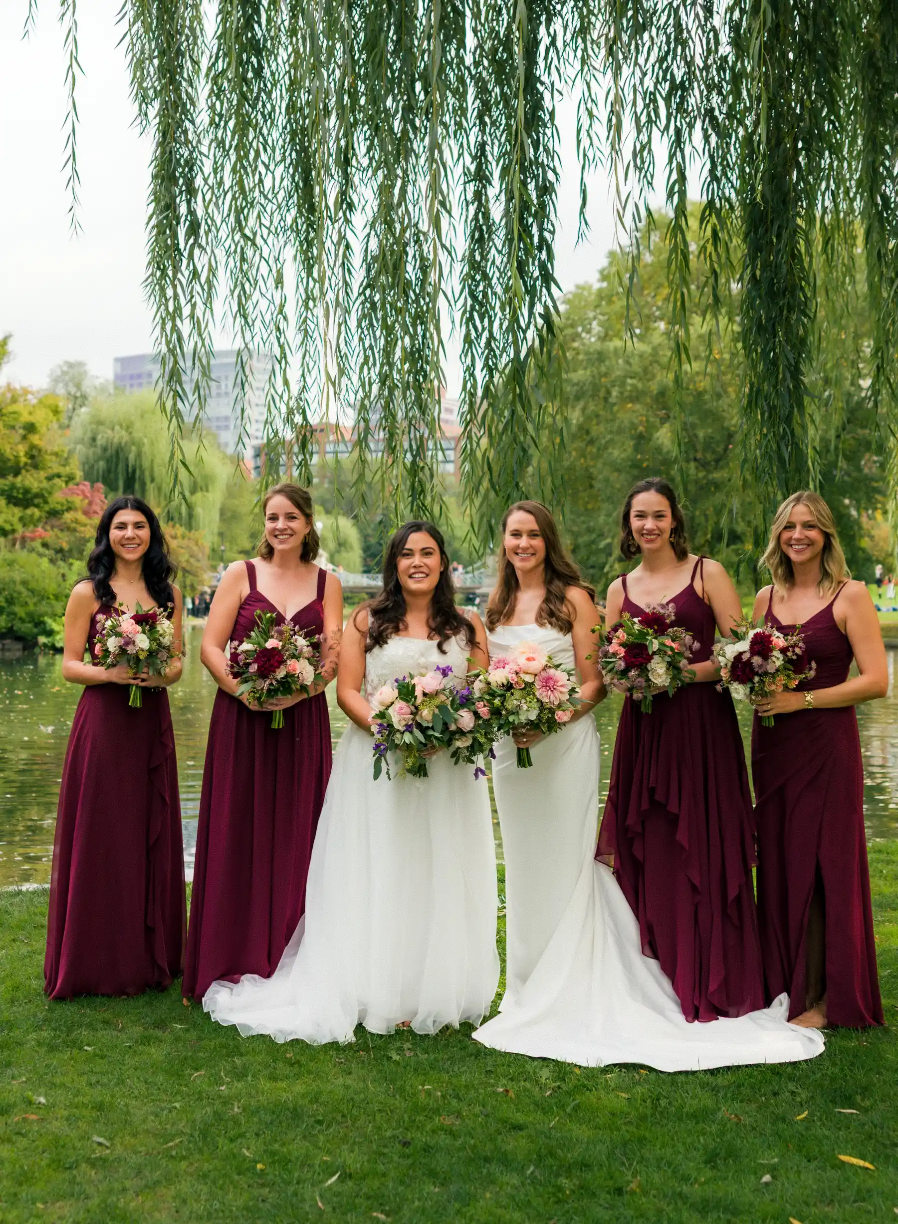 Brides Ashton Hattori and Stephanie Tillman pose with four bridesmaids in burgundy gowns under a weeping willow in Boston.