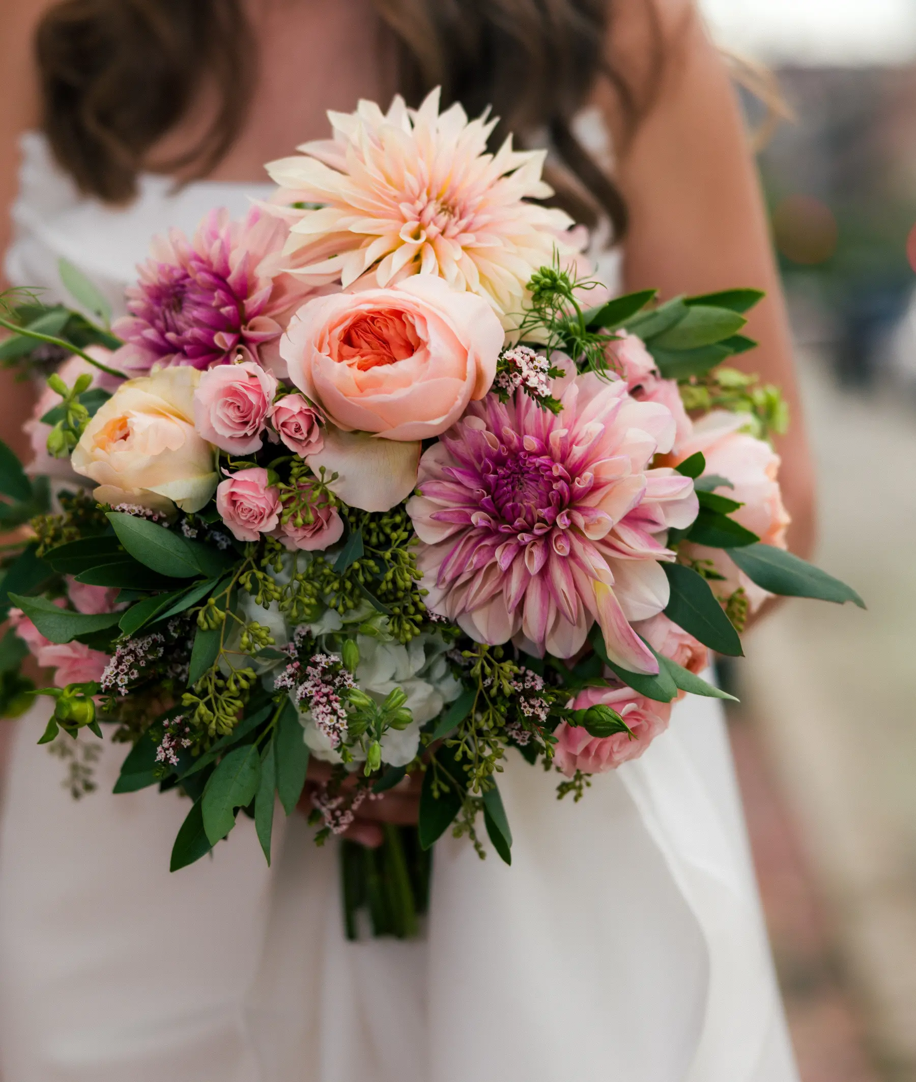 A bride in a white gown holds a lush bridal bouquet of pink and peach dahlias, garden roses and greenery at Hampshire House in Boston.