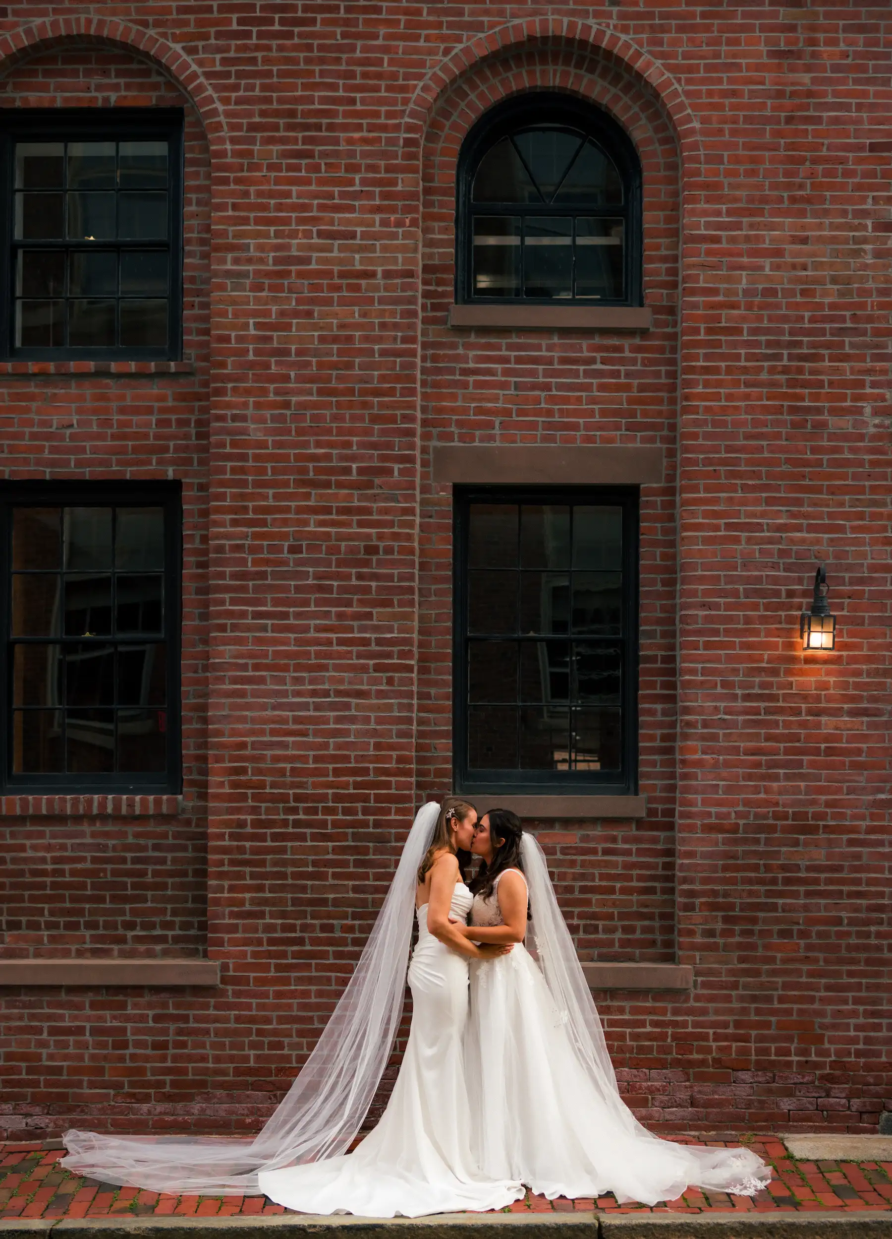 Brides Ashton Hattori and Stephanie Tillman share a kiss in white gowns and veils outside Hampshire House in Boston.
