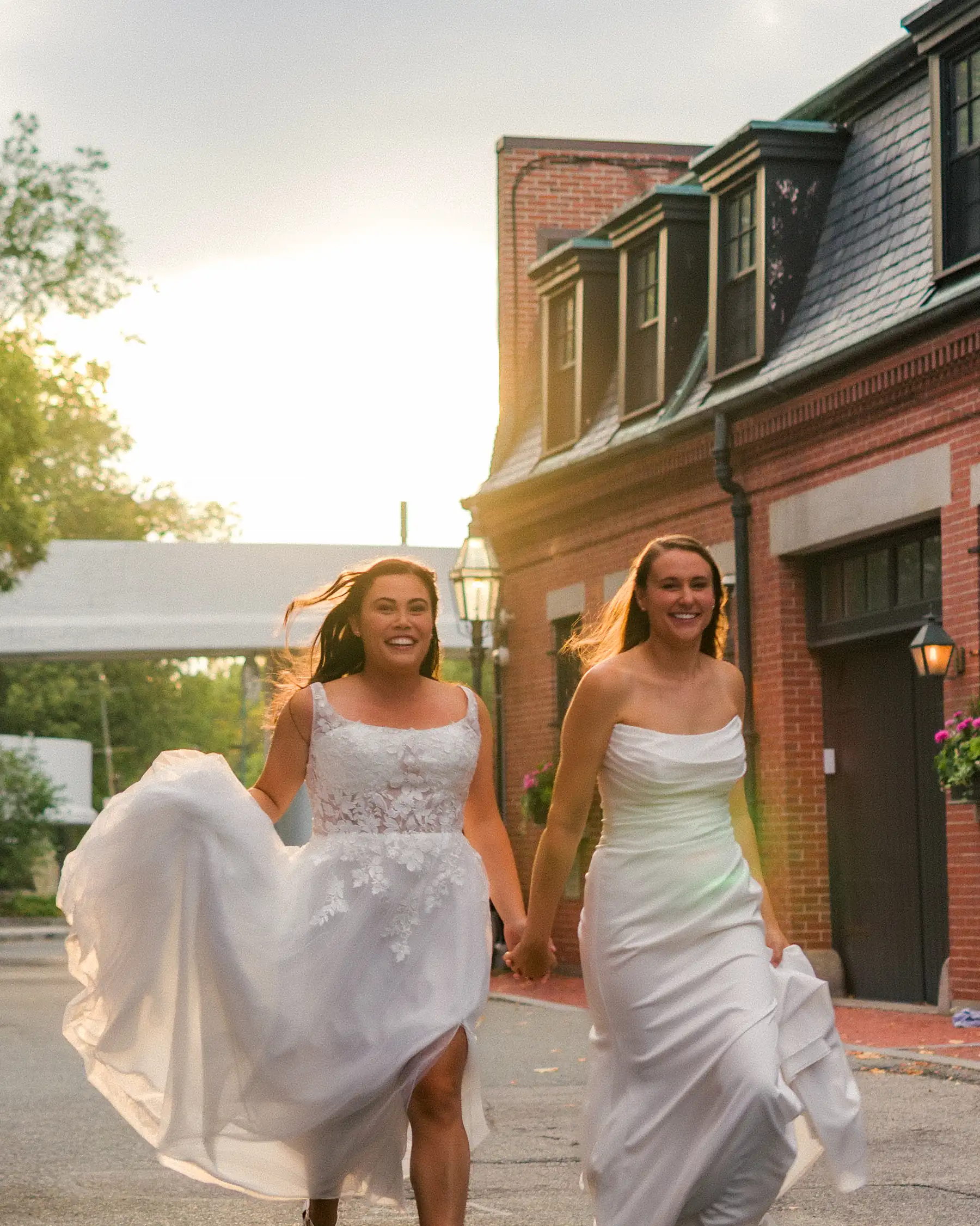 Brides Ashton Hattori and Stephanie Tillman run hand-in-hand in white gowns outside Hampshire House in Boston.