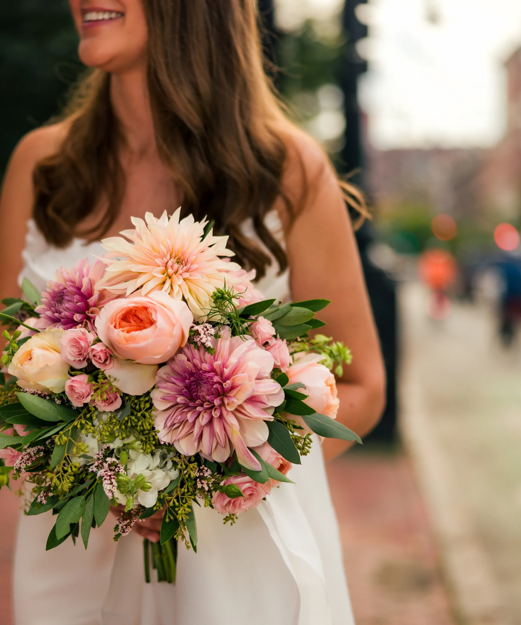 Bride Ashton Hattori smiles while holding a lush pink and peach bridal bouquet with dahlias and garden roses at Hampshire House in Boston.