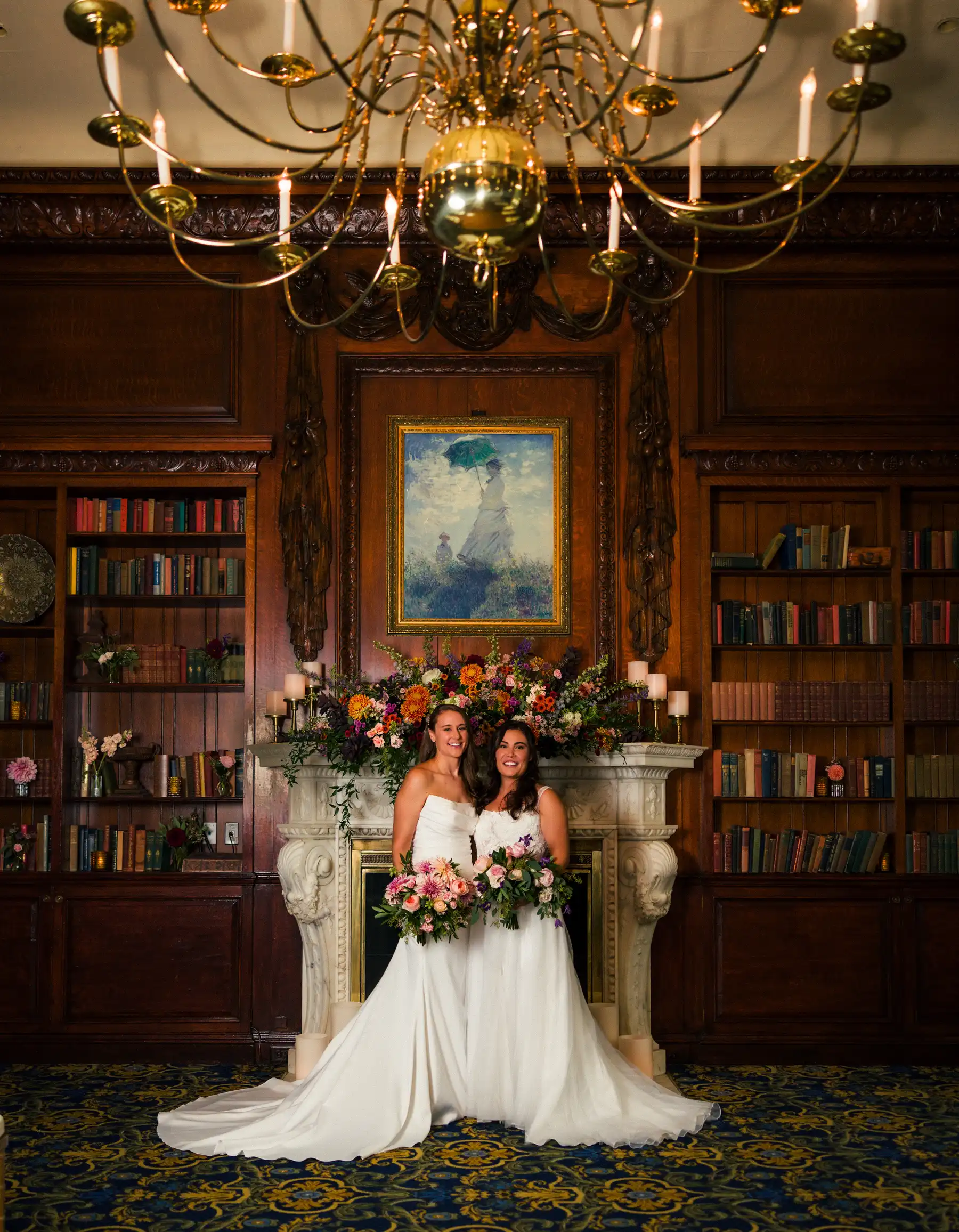 Brides Ashton Hattori and Stephanie Tillman pose in white gowns before a floral-adorned fireplace at Hampshire House, Boston.