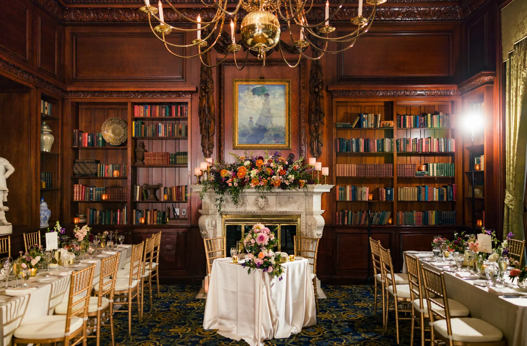 Elegant library reception room at Hampshire House in Boston with floral arrangements, gold chiavari chairs and candlelit bookshelves.