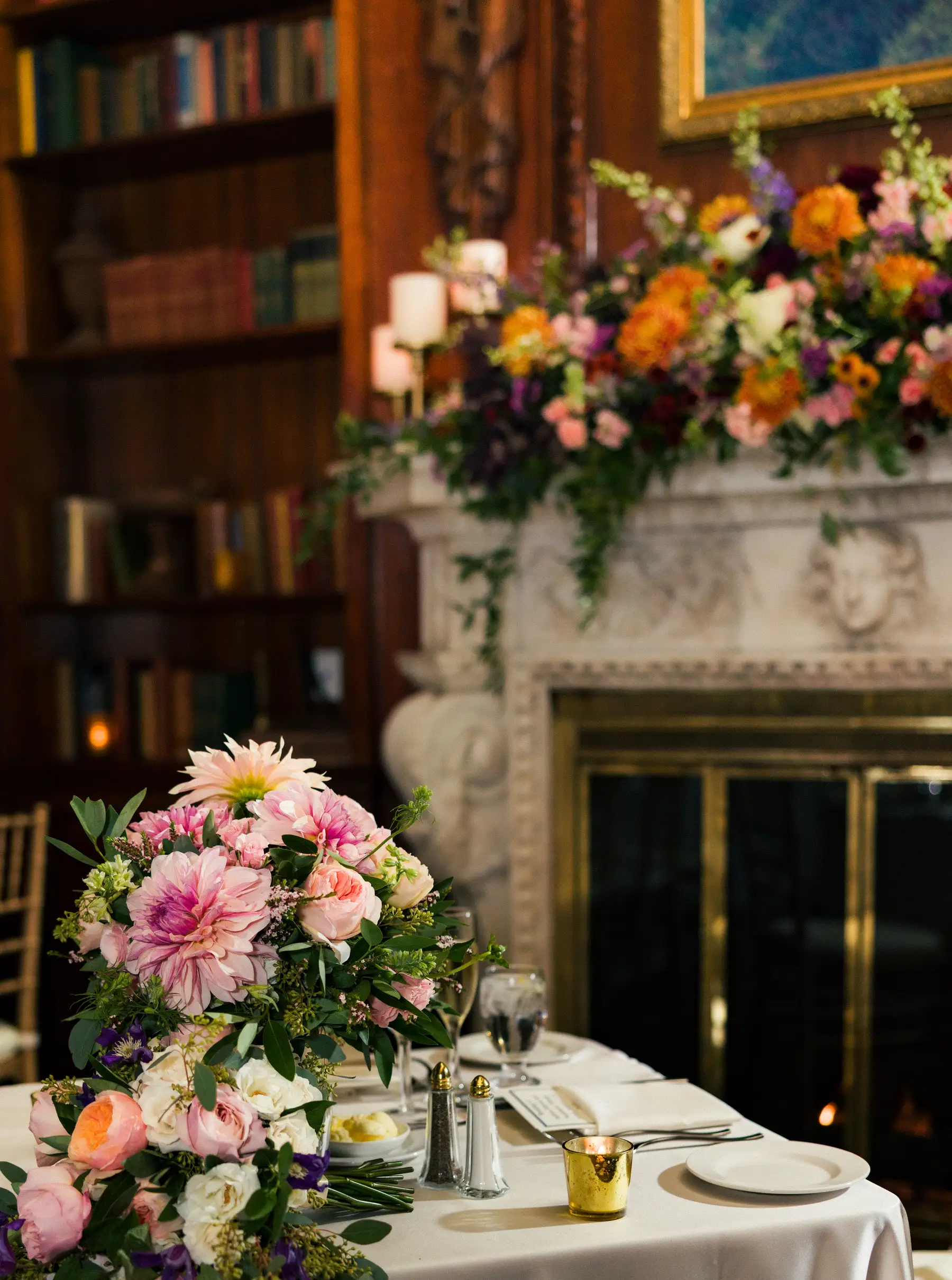 Lush pink and coral floral centerpiece on a dinner table at Hampshire House in Boston, with a flower-draped fireplace behind it.
