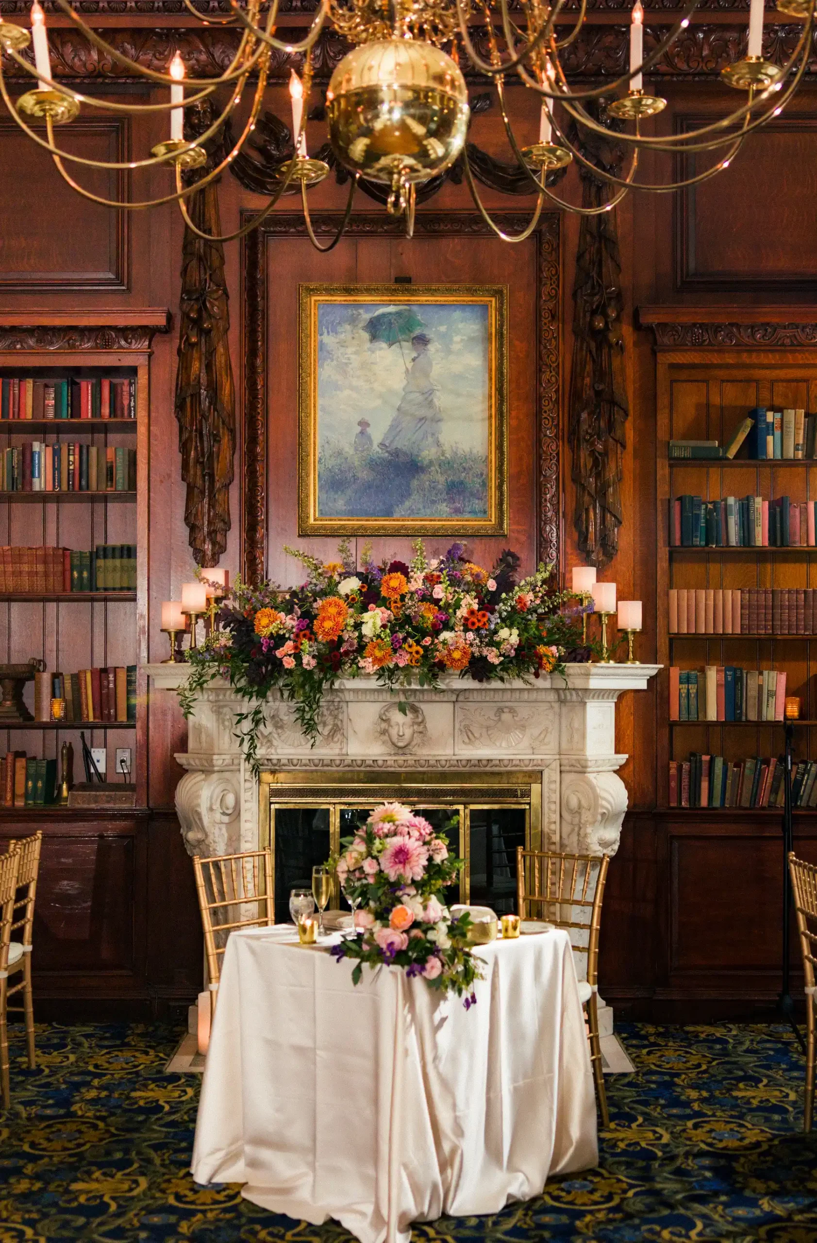 Sweetheart table with floral centerpiece in front of ornate fireplace and bookshelves at Hampshire House, Boston.