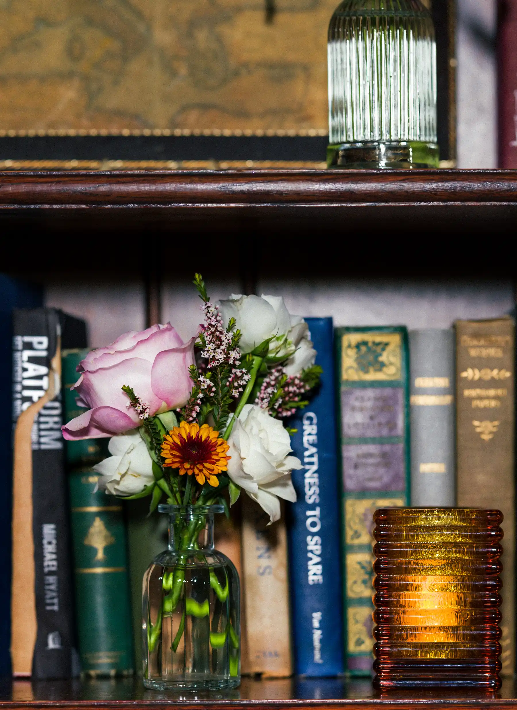A small glass vase of pink roses and wildflowers sits among vintage books on a shelf at Hampshire House in Boston.