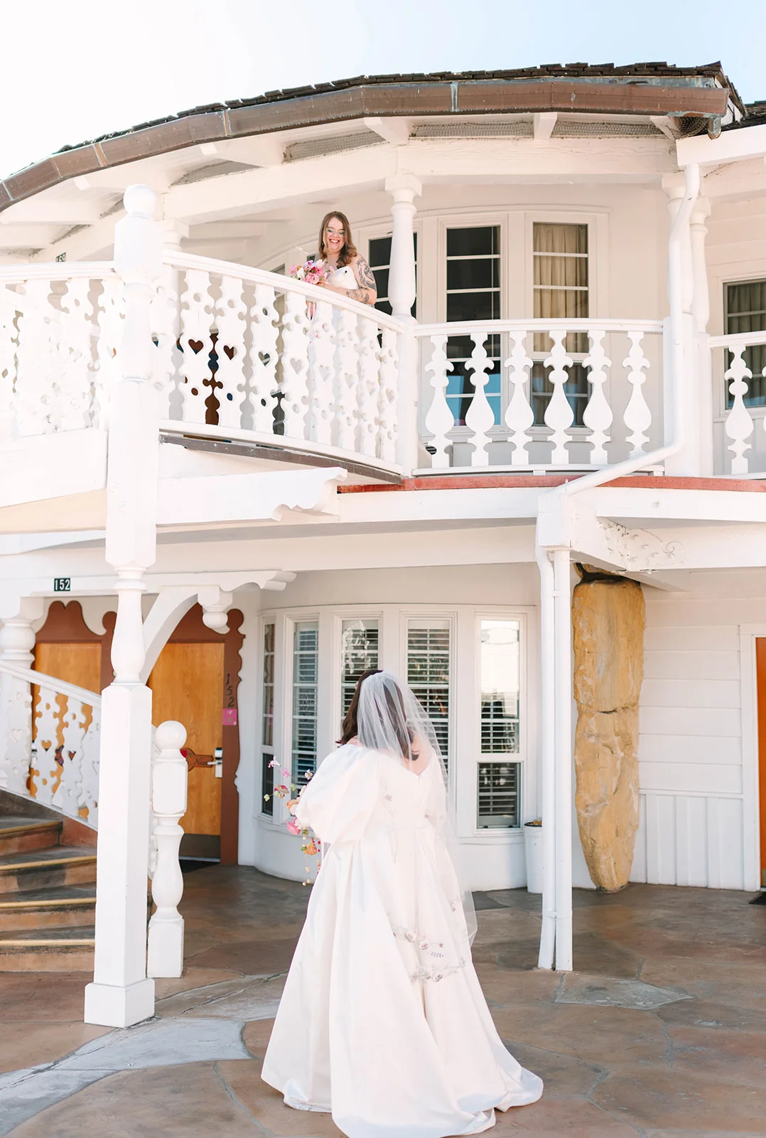 Bride Mimi in a white gown and veil looks up at bridesmaid Courtney on the balcony of the Madonna Inn in San Luis Obispo.