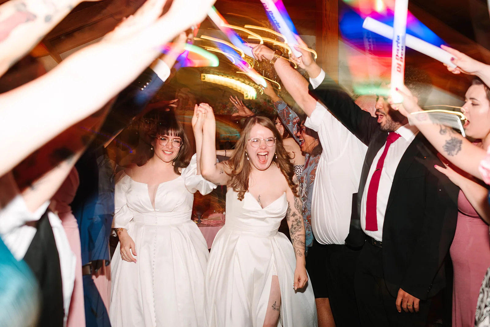 Brides Mimi and Courtney run through a glow stick tunnel with cheering guests at Madonna Inn in San Luis Obispo.