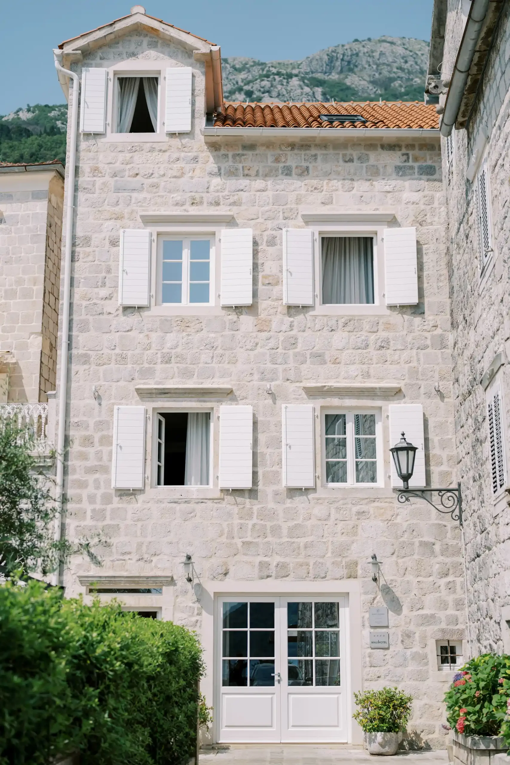Stone facade of Monte Bay Retreat in Perast, Montenegro, with white shutters and terracotta roof tiles.